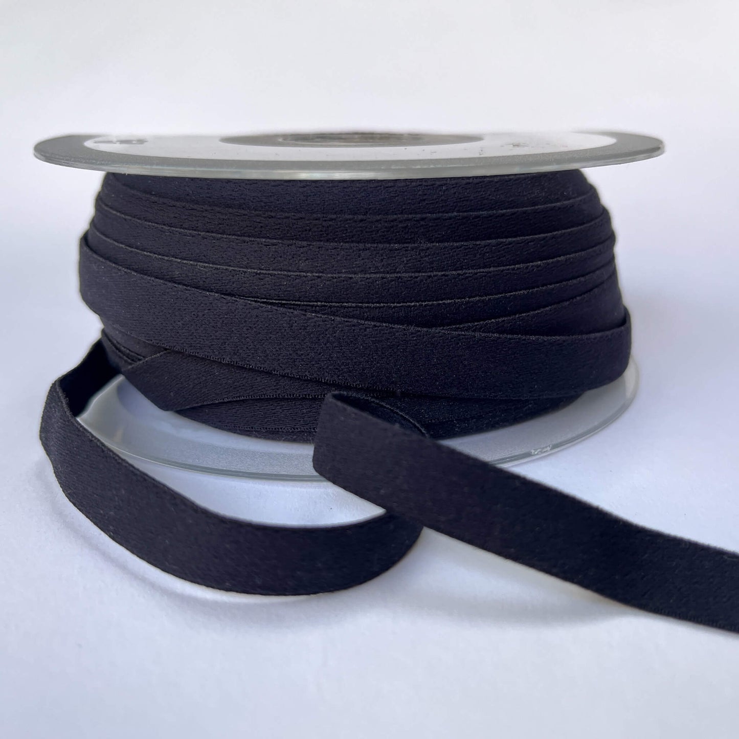 A spool of wide black elastic ribbon with a length of the ribbon unspooled in front, set against a plain white background.
