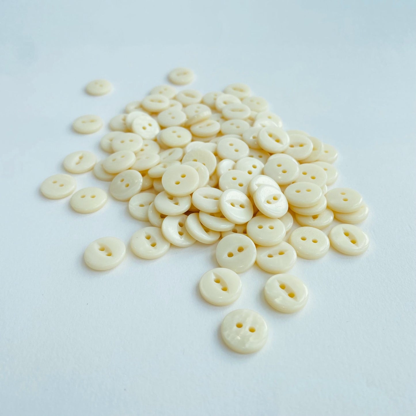 Fisheye Codelite Dairy Shirt Buttons - Kleins Haberdashery, a pile of plastic free Natural Pearlescent buttons made from milk on a white background