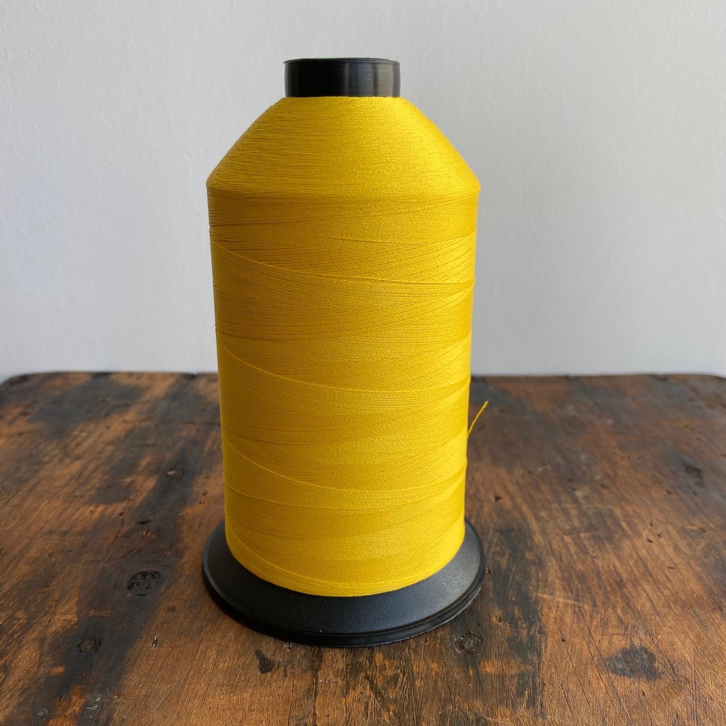 Large spool of yellow thread on a wooden surface with a white background
