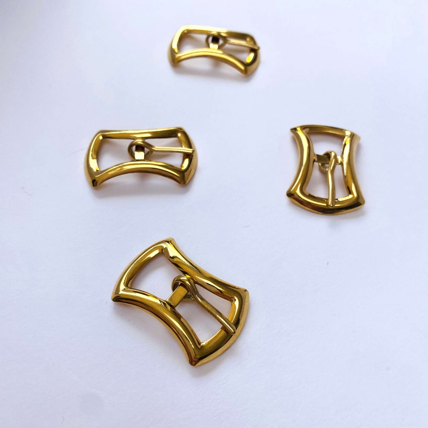 Gold Curved Prong Buckle - 8mm Four unusual shaped gold buckles arranged on a white background