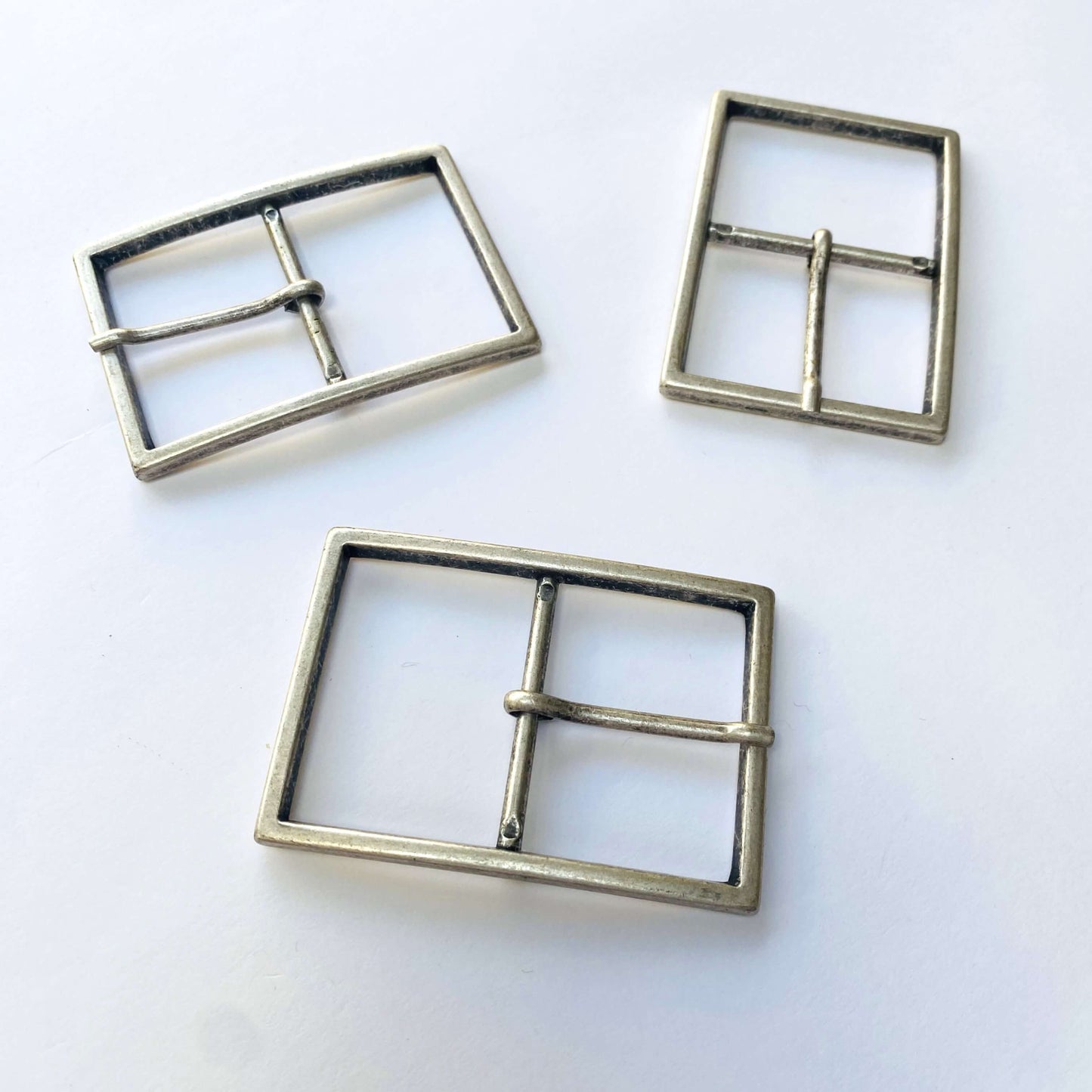 Three large antique silver metal belt buckles with prongs on a white background