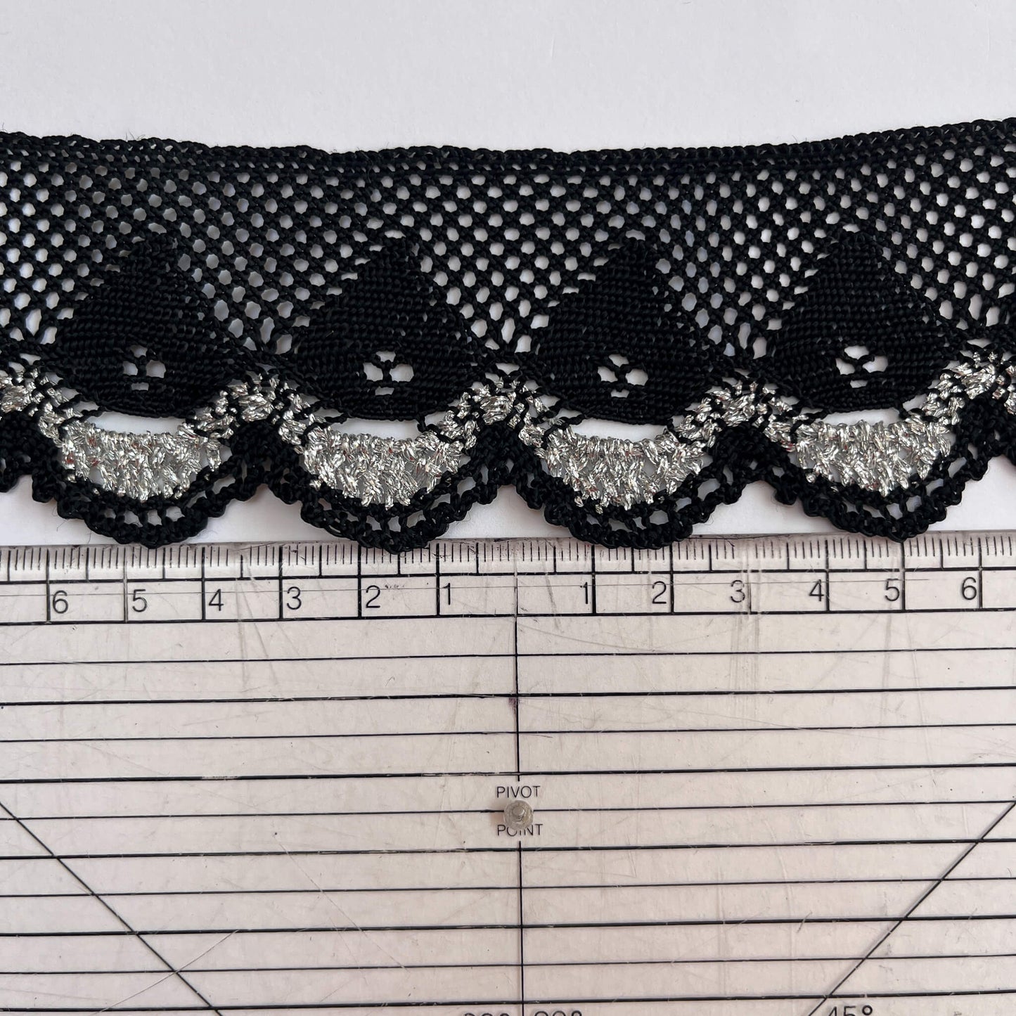Black lace trim with silver accents on a white background with a ruler for scale.