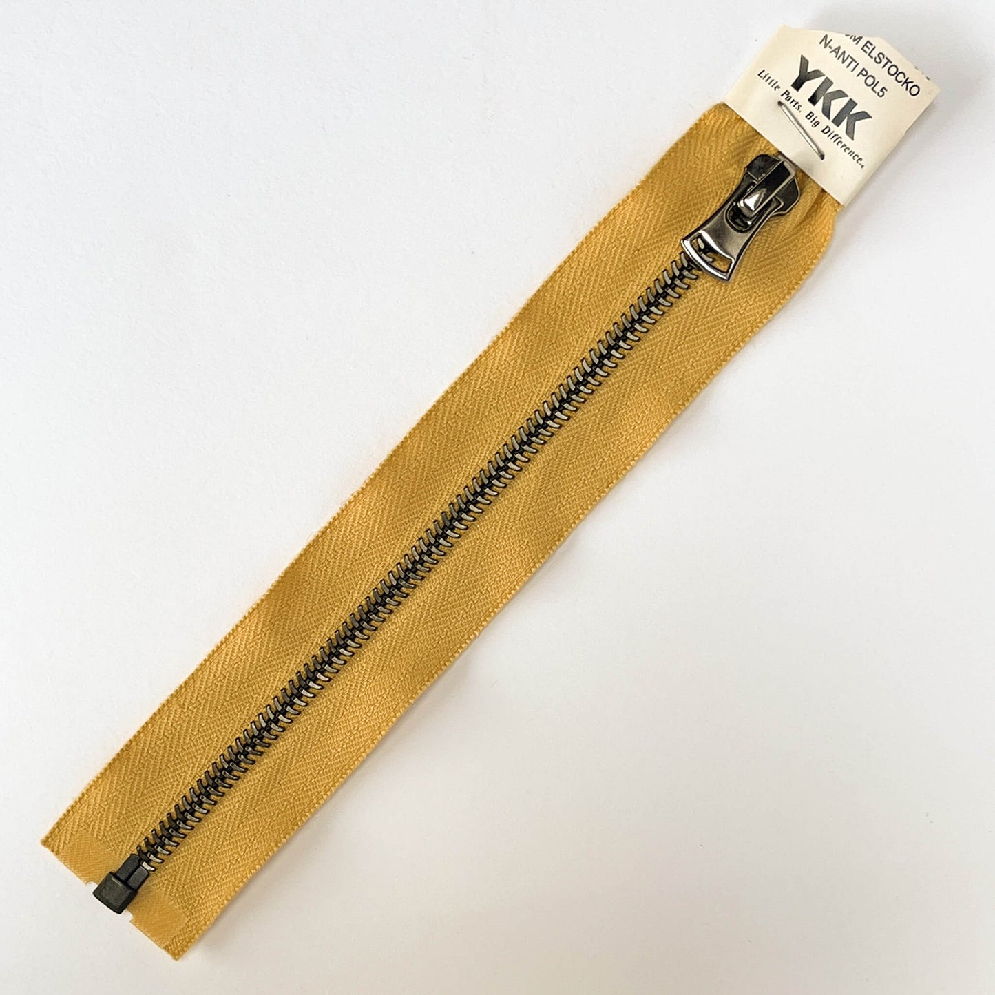 A YKK EXCELLA® Blade zip open end zip with mustard tape, 'herringbone' style black-silver metal teeth and decorative puller.