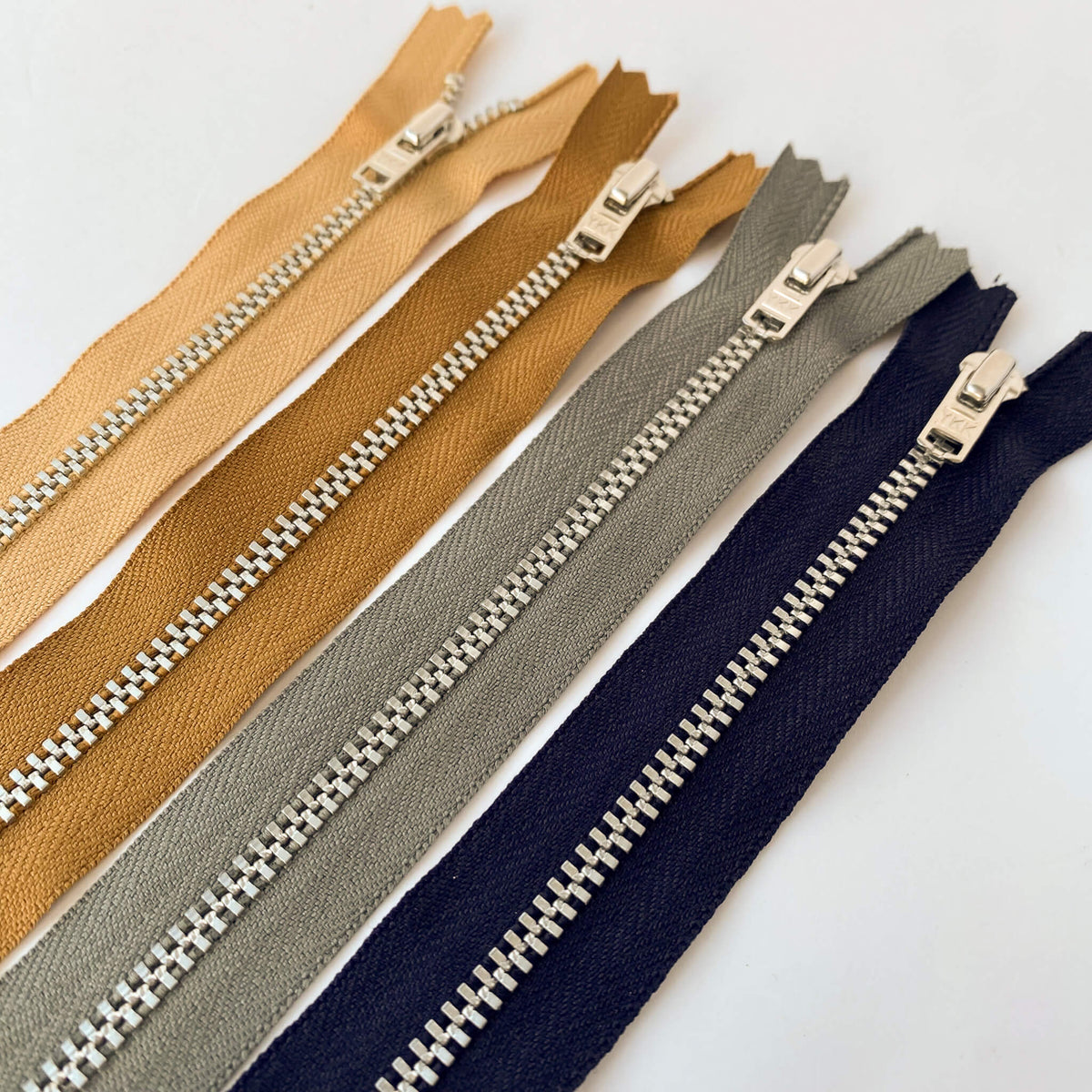 YKK jeans zip with silver metal teeth and auto-lock puller in various shades of brown, blue and grey