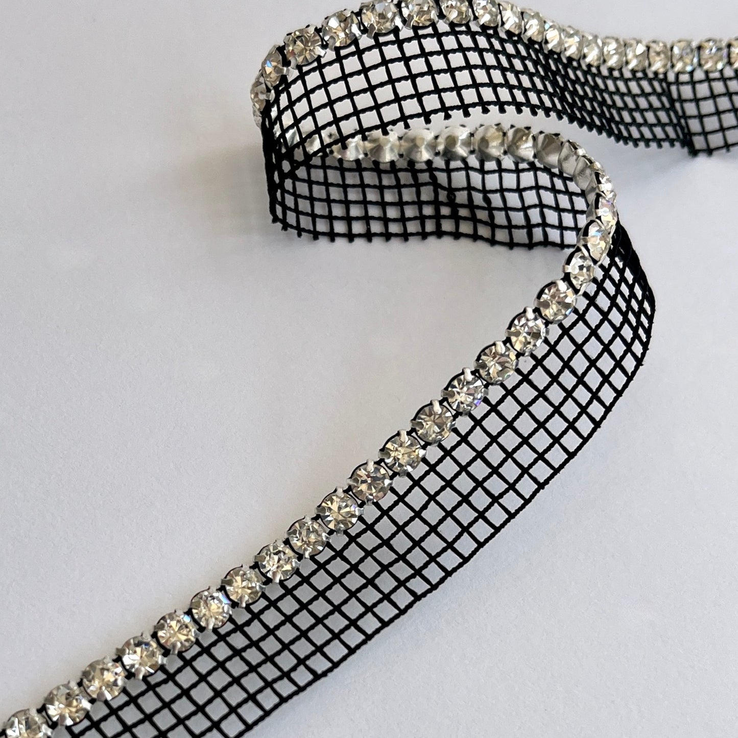Sparkly rhinestone insertion trim - premium high grade diamanté crystals on a flexible net insertion tape. Please note - we have very limited stock of the white colour way. Black/clear crystal: Sold by the metre White/clear crystal: LIMITED STOCK - 80cm length only