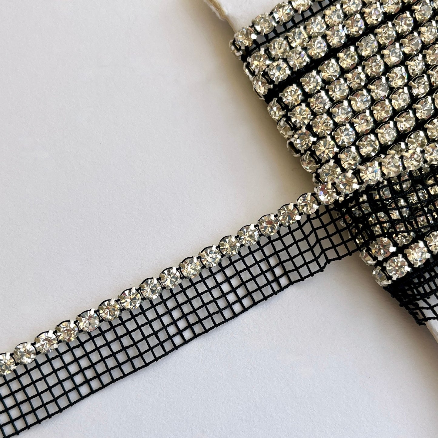 Sparkly rhinestone insertion trim - premium high grade diamanté crystals on a flexible net insertion tape. Please note - we have very limited stock of the white colour way. Black/clear crystal: Sold by the metre White/clear crystal: LIMITED STOCK - 80cm length only