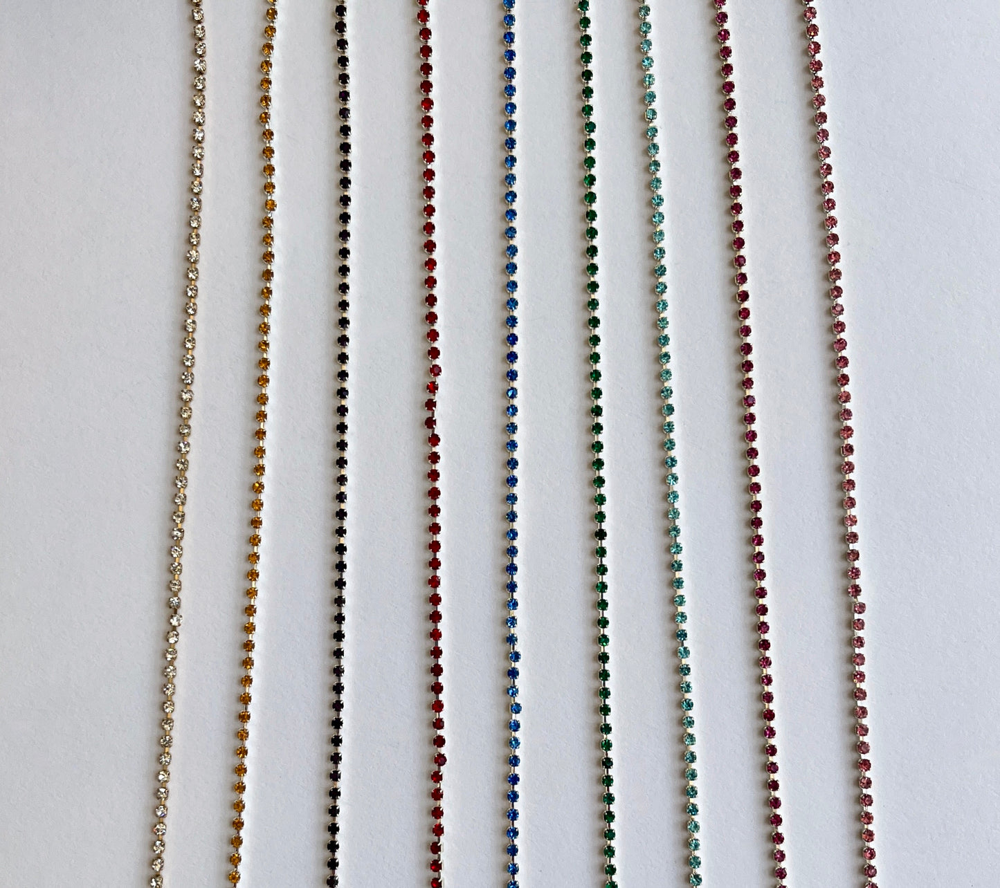 Delicate rhinsteone trim - premium high grade coloured diamante crystals set in a flexible metal chain casing SOLD BY THE METRE Colours: gold-clear crystal, silver-saffron, silver-Amethyst (dark purple), silver-red, silver-sapphire, silver-emerald, silver-aqua, silver-fuchsia, silver-rose Approx Overall Width: 3mm (⅛”) Stone Size: SS4.5