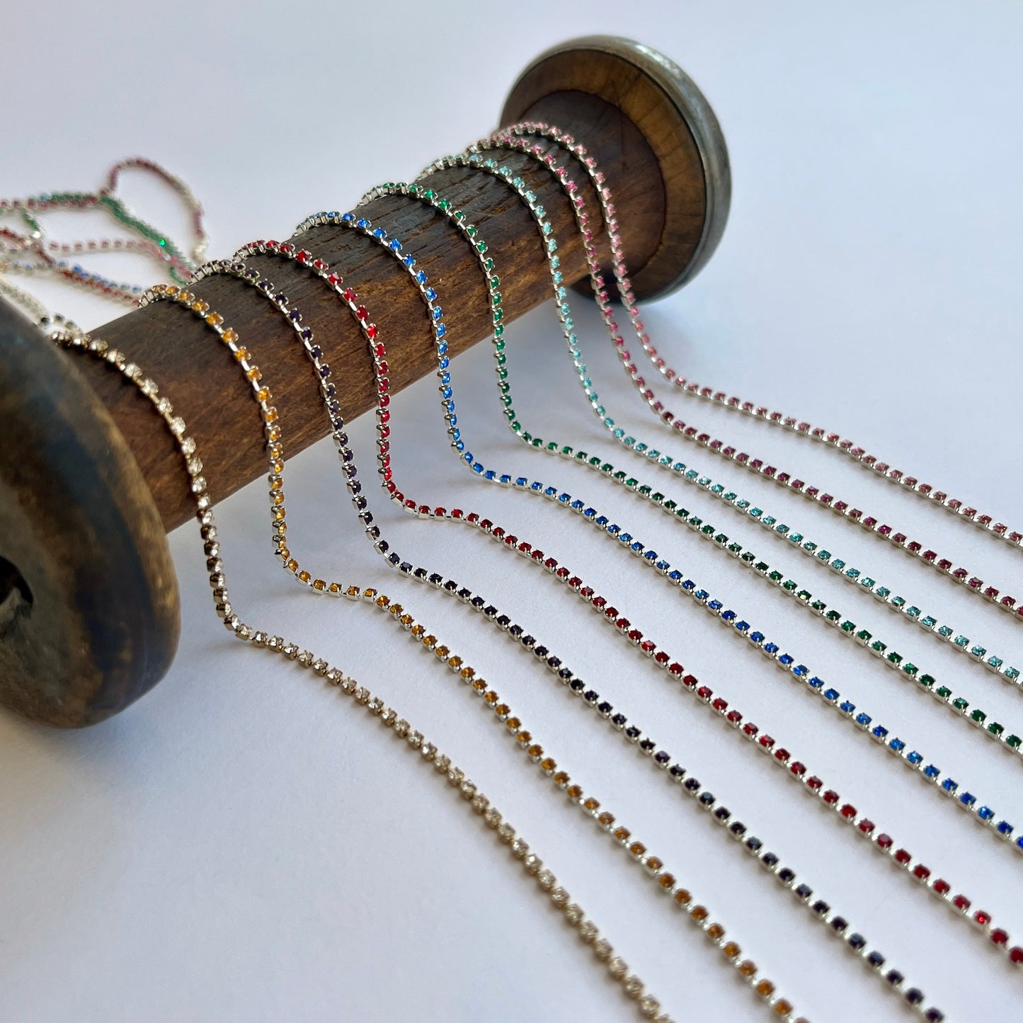 Delicate rhinsteone trim - premium high grade coloured diamante crystals set in a flexible metal chain casing SOLD BY THE METRE Colours: gold-clear crystal, silver-saffron, silver-Amethyst (dark purple), silver-red, silver-sapphire, silver-emerald, silver-aqua, silver-fuchsia, silver-rose Approx Overall Width: 3mm (⅛”) Stone Size: SS4.5
