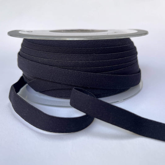 A spool of wide black elastic ribbon with a length of the ribbon unspooled in front, set against a plain white background.