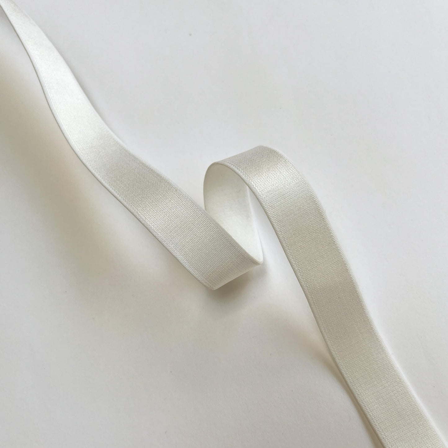 A close-up of a wide, off-white satin ribbon with a soft sheen, elegantly draped and looped on a clean, light background.