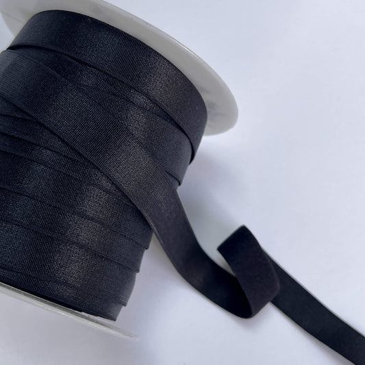 A close-up of a spool of black satin ribbon with a length of the ribbon unwound, set against a plain white background.
