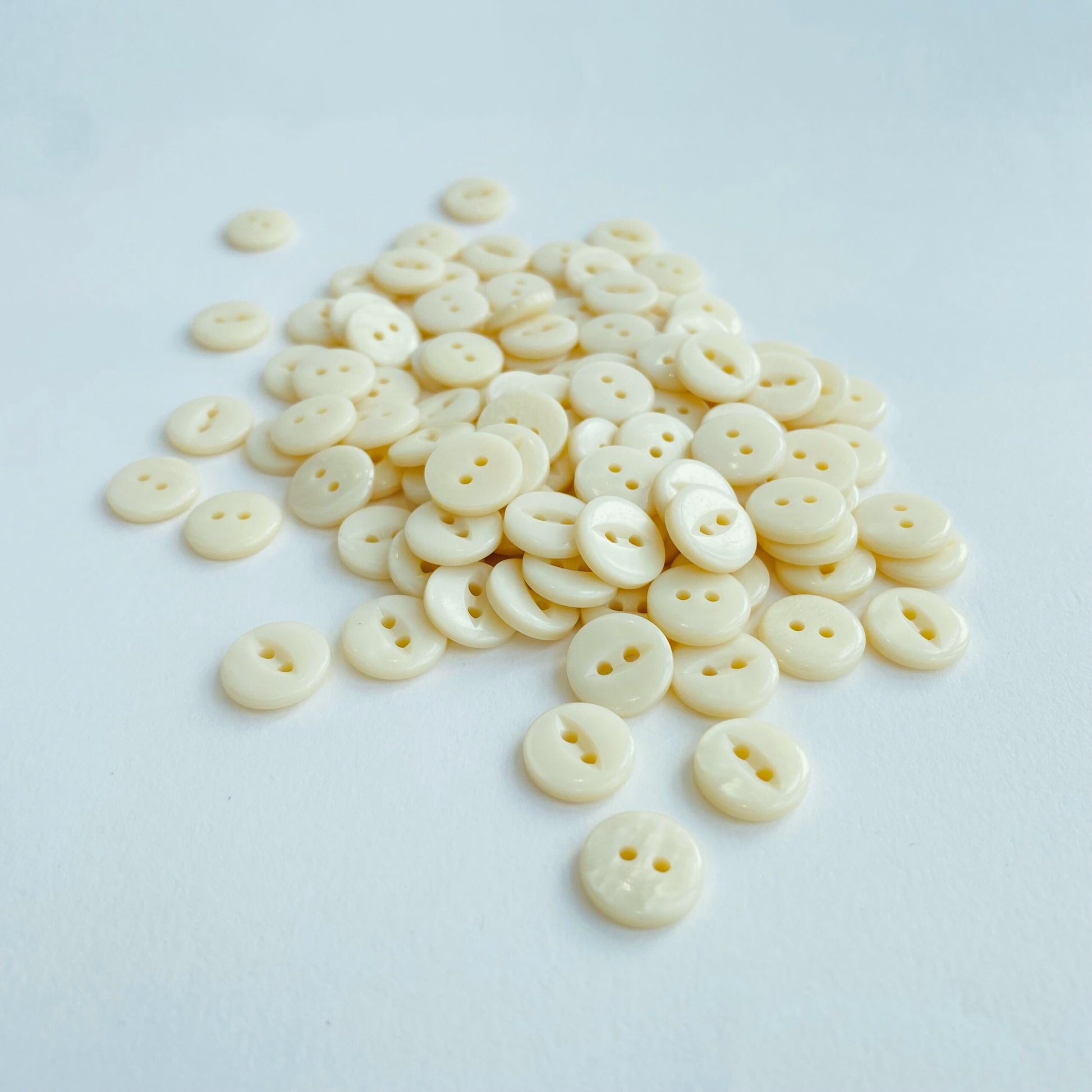 Fisheye Codelite Dairy Shirt Buttons - Kleins Haberdashery, a pile of plastic free Natural Pearlescent buttons made from milk on a white background