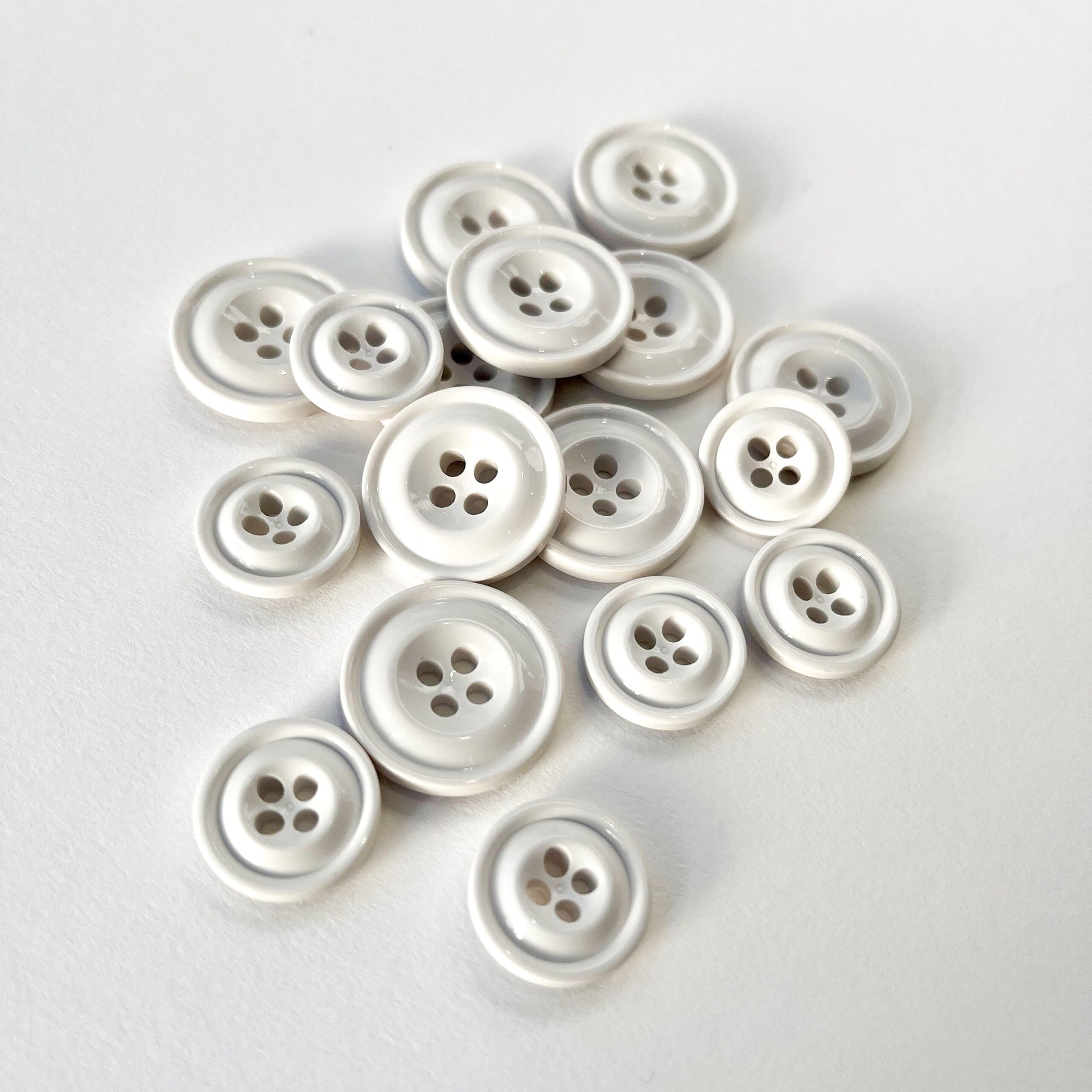 A group of white 4 hole Codelite buttons of various sizes, with one button standing upright in the foreground on a clean white background. Codelite buttons - plastic free, organic & sustainable.