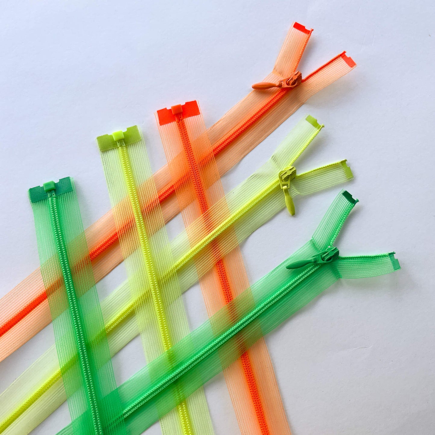 Translucent mesh zippers in assorted bright colours including green, orange, yellow arranged diagonally on a plain white background. Couture Featherweight open ended zip - 100cm length.