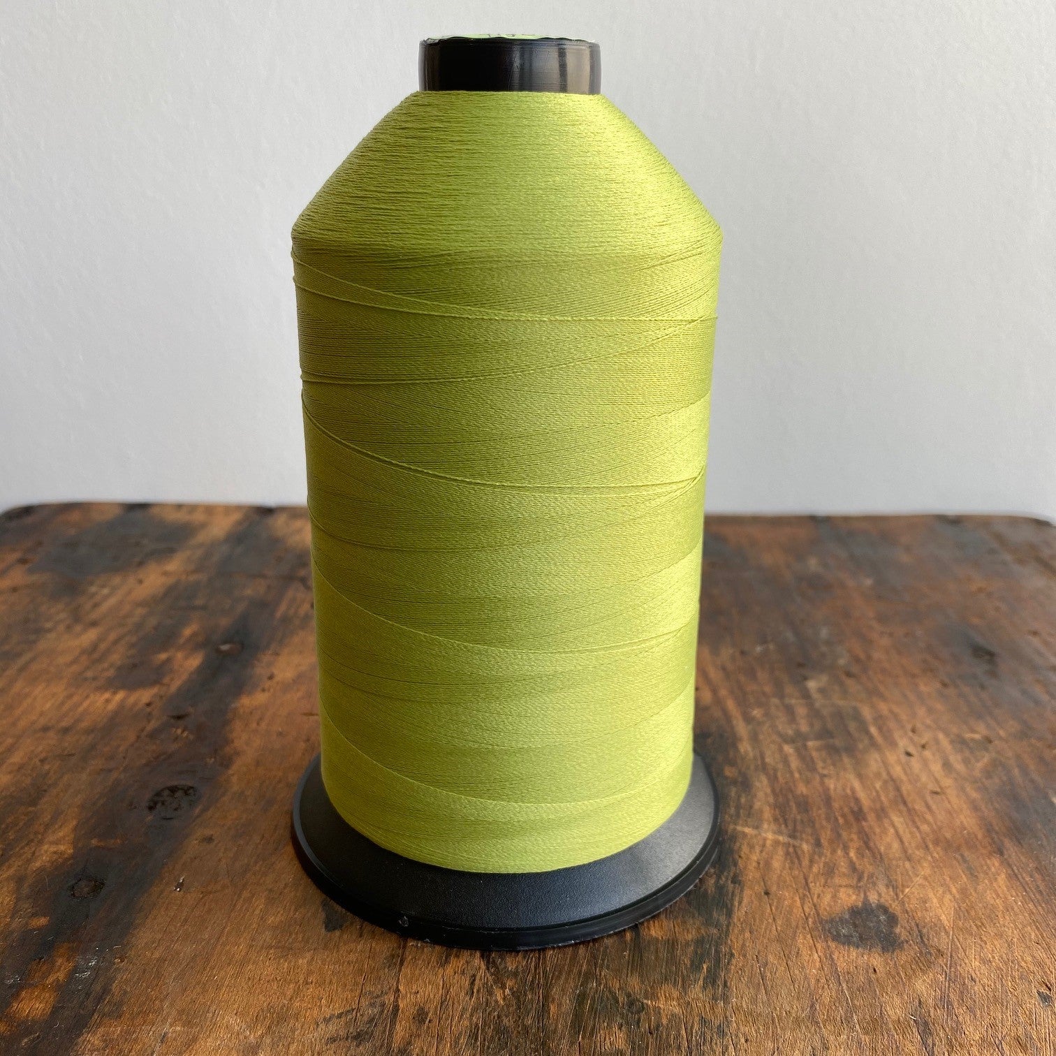 Large spool of green thread on a wooden surface with a white background