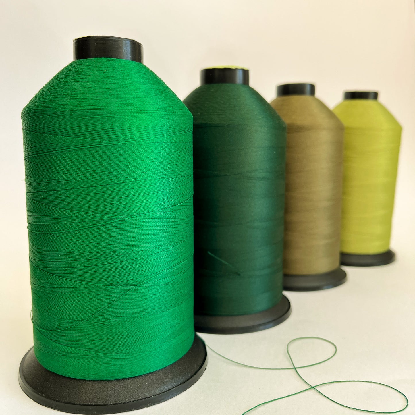 Four spools of green thread in different shades on a light background