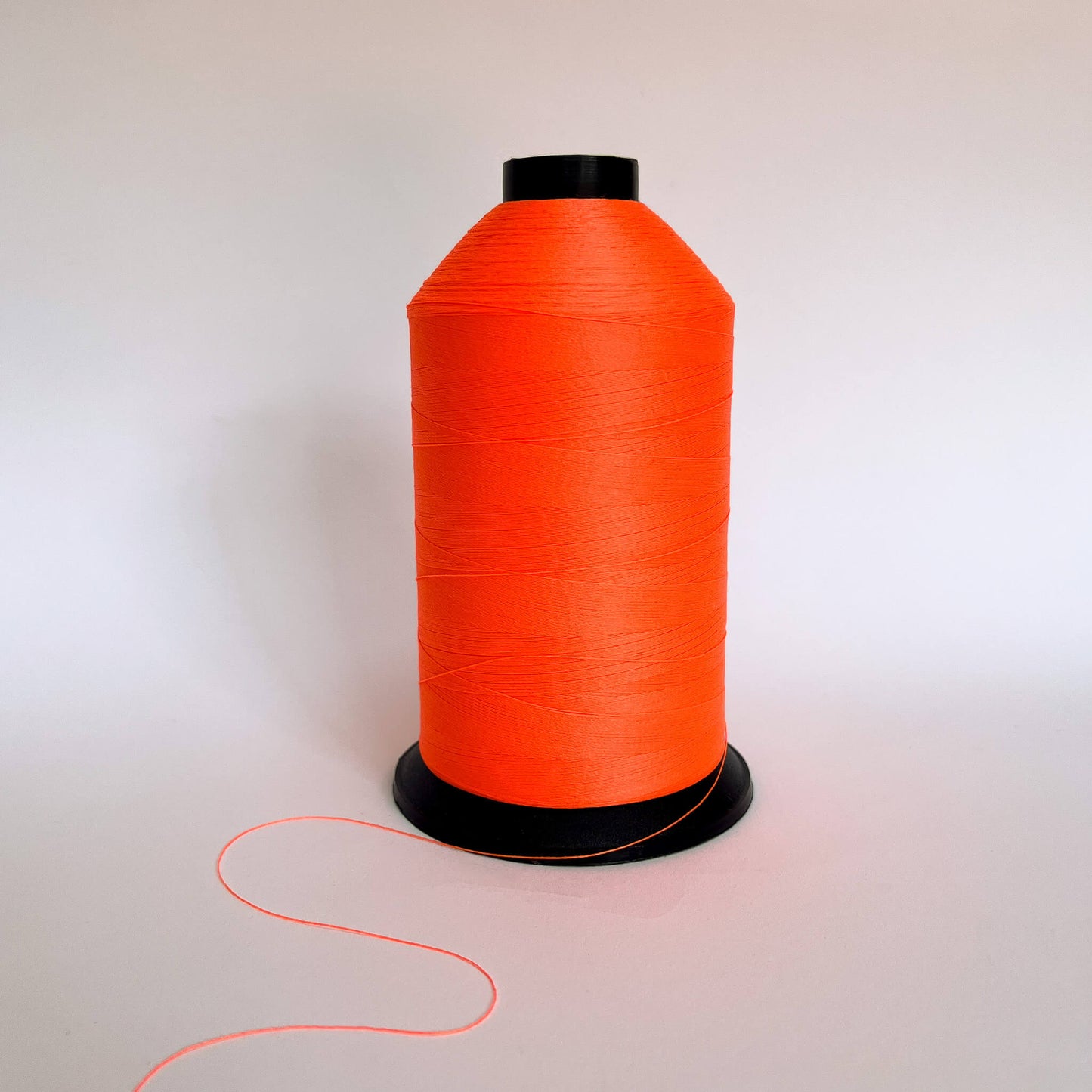 A large spool of bright neon orange thread standing upright on a plain white background with a short tail of thread visible in the foreground.