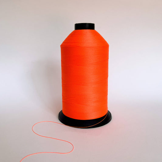 A large spool of bright neon orange thread standing upright on a plain white background with a short tail of thread visible in the foreground.