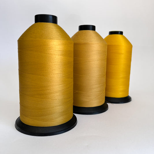 Three spools of gold, mustard, yellow thread on a white background 
