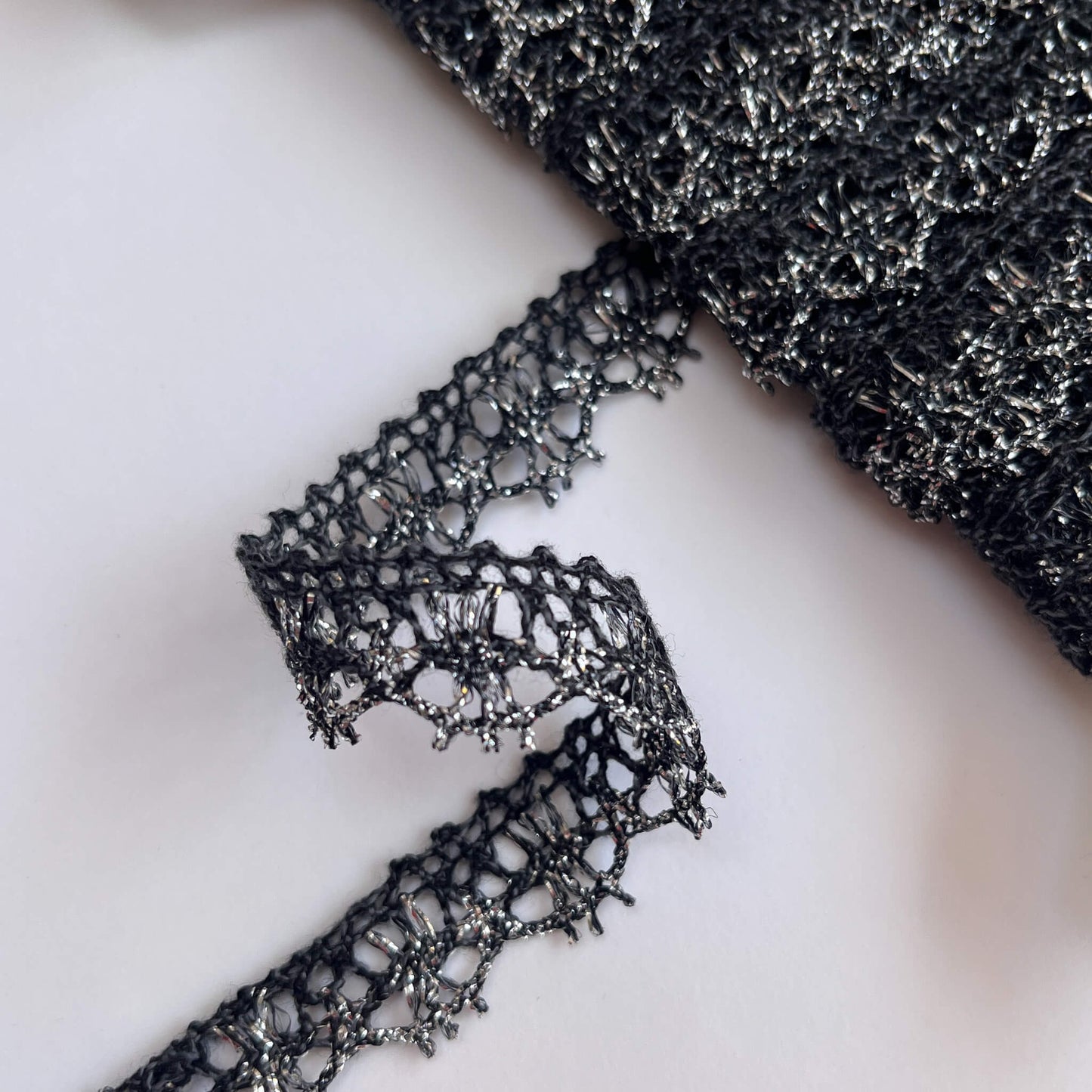 Close-up of grey and silver Nottingham lace trim on a white background