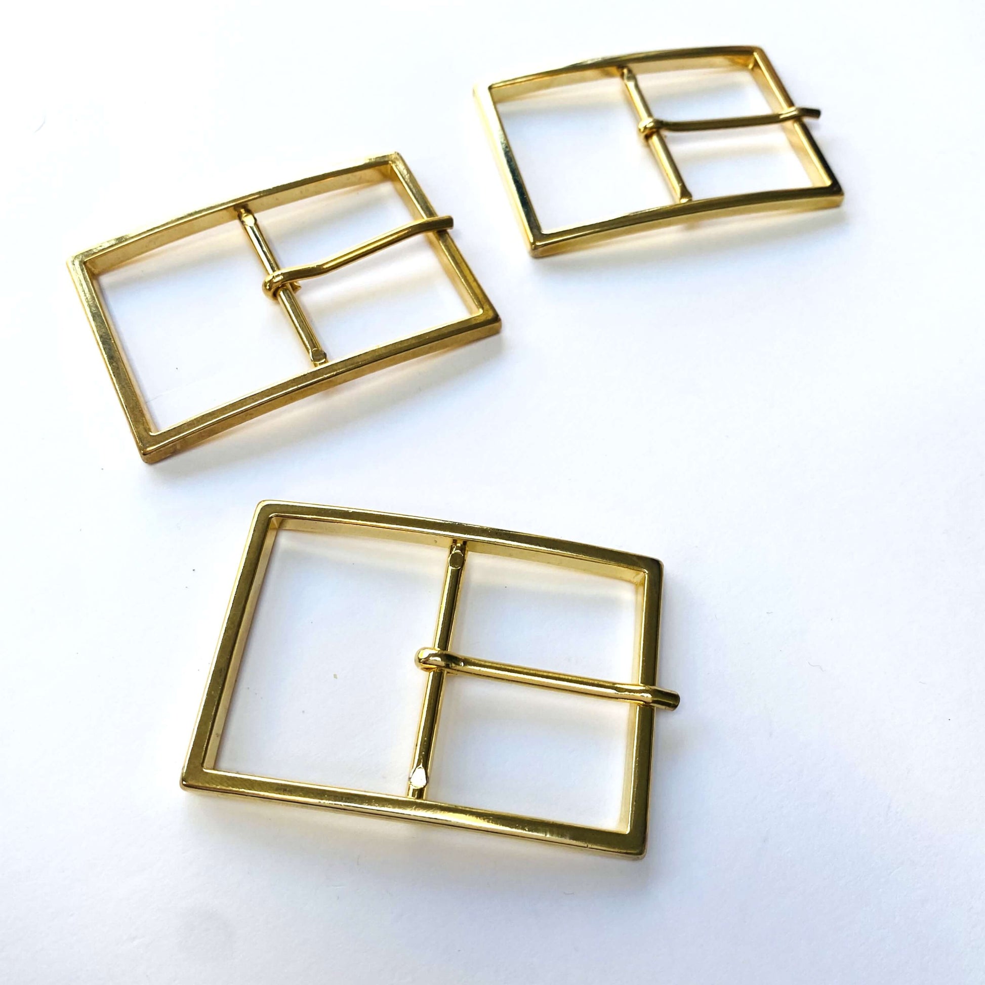 Three large gold square coat buckles with prongs on a white background
