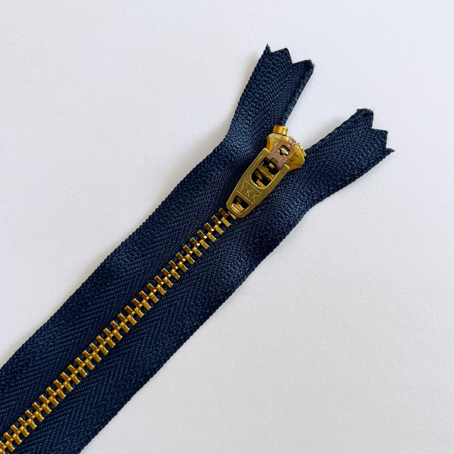 Navy blue zipper with gold metal zipper pull on a white background