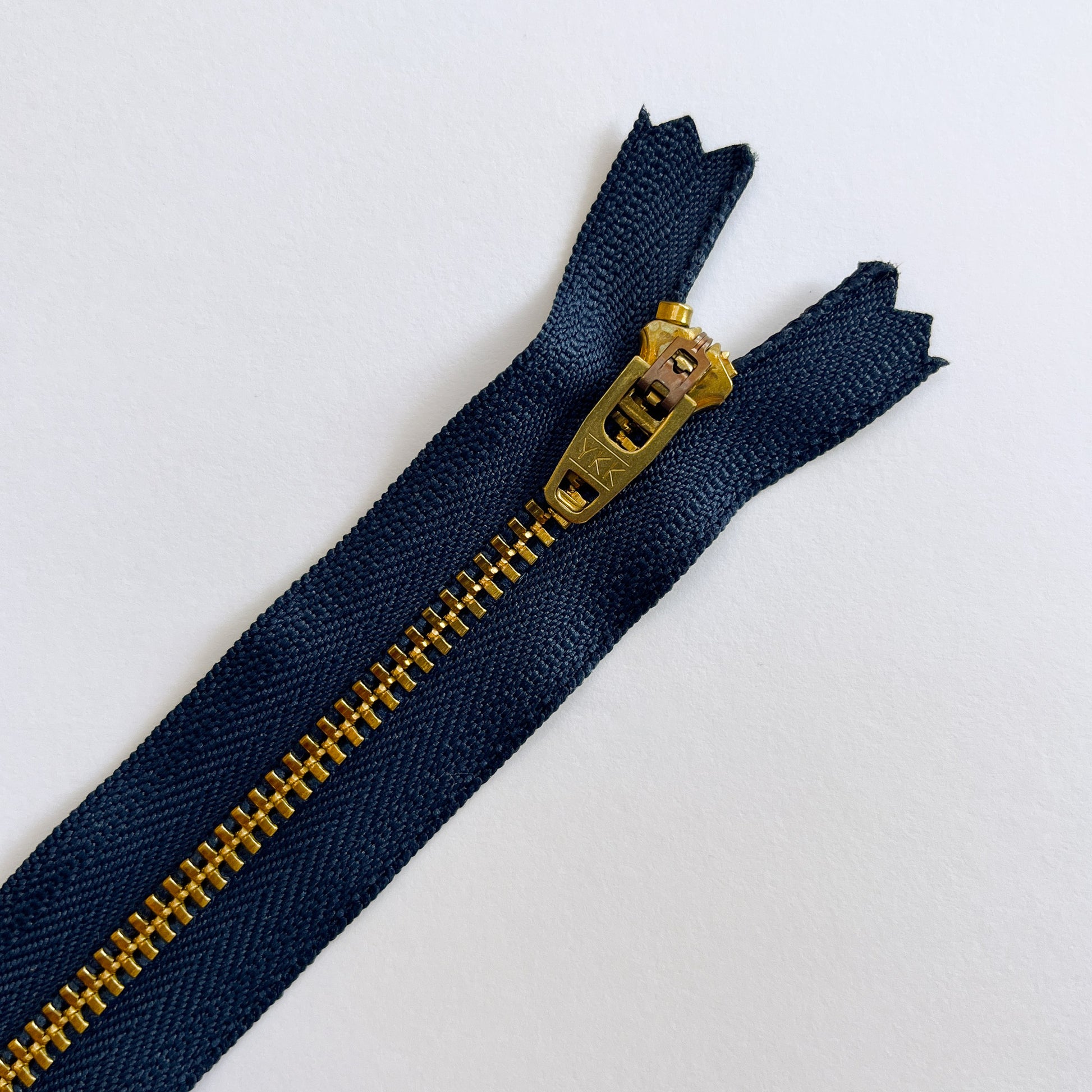 Navy blue zipper with gold metal zipper pull on a white background