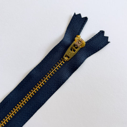 Navy blue zipper with gold metal zipper pull on a white background