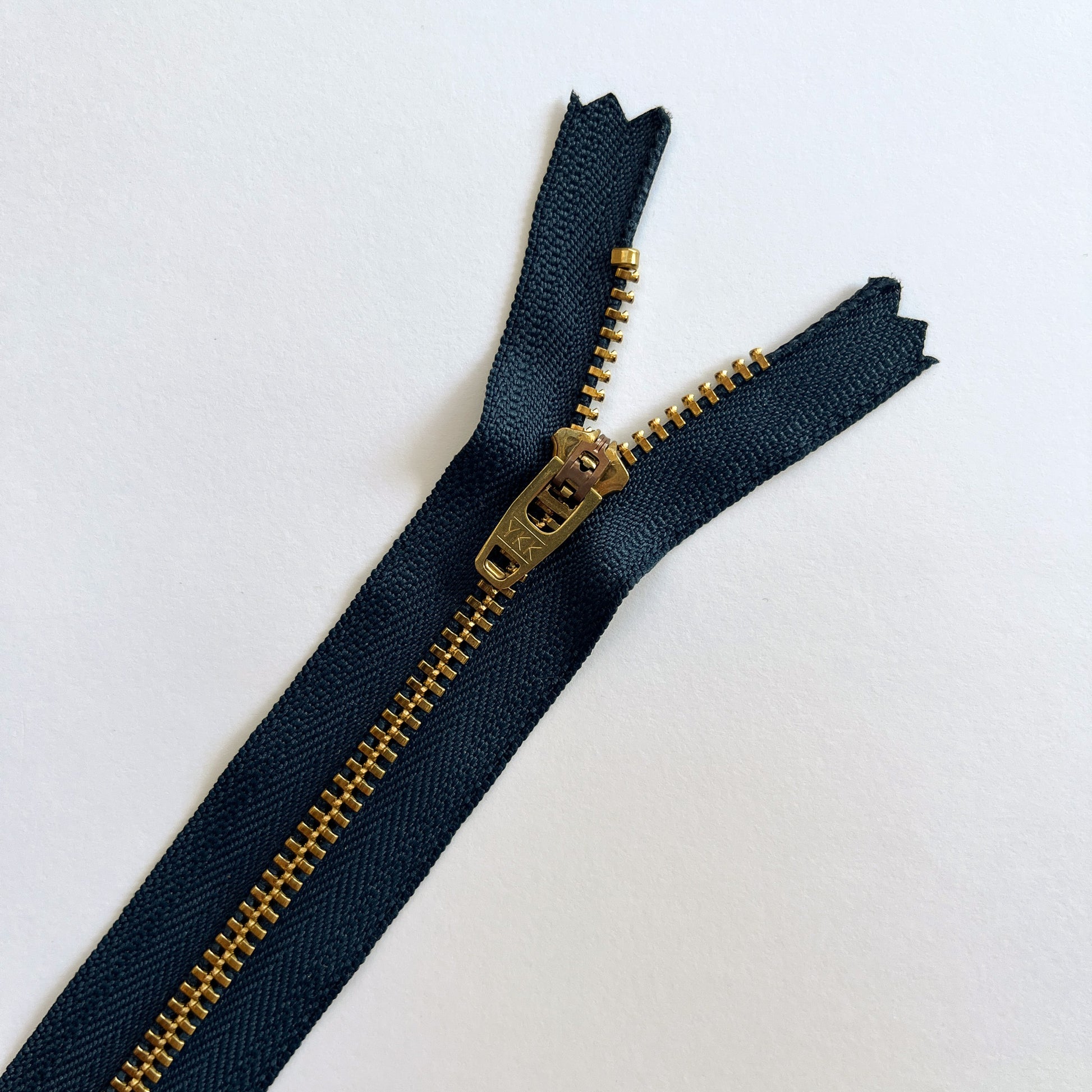 Navy blue zipper with brass metal zipper pull on a white background