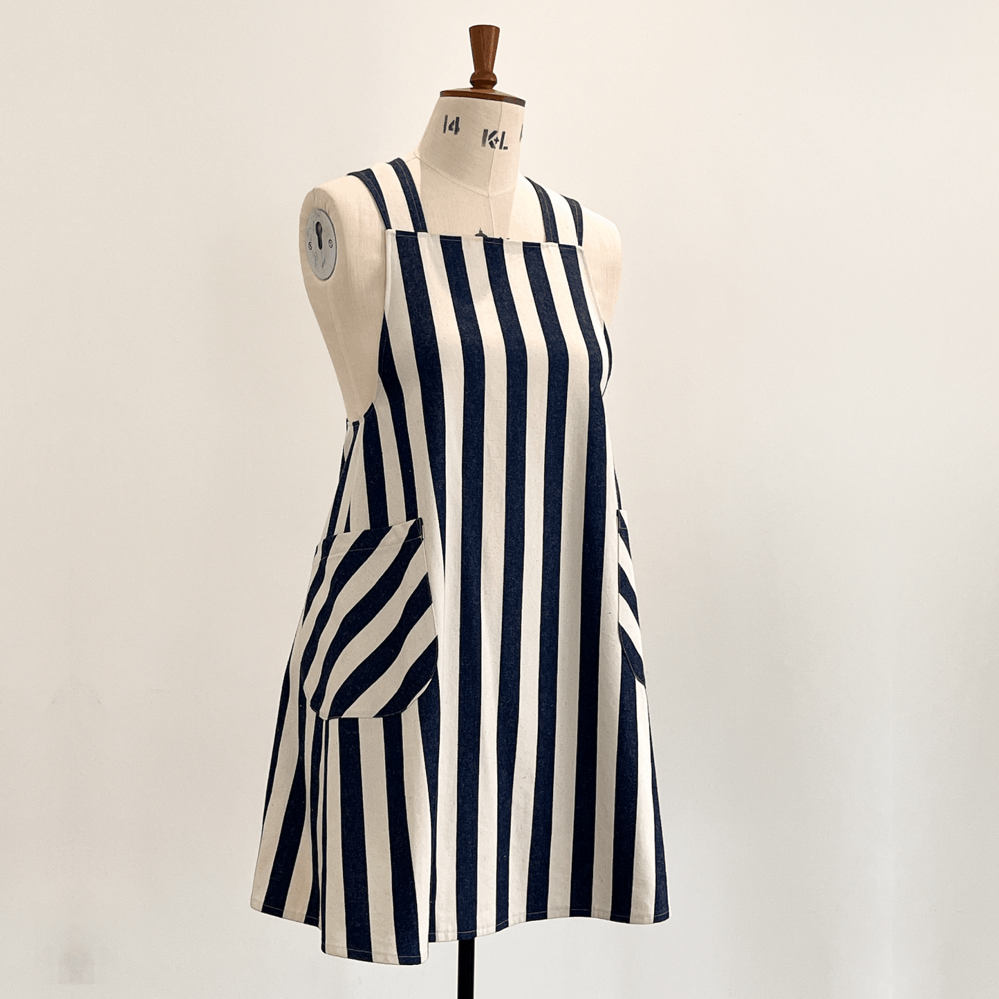 A Japanese style apron with vertical navy blue and off-white stripes, displayed on a cream-coloured dress form mannequin against a plain light background.