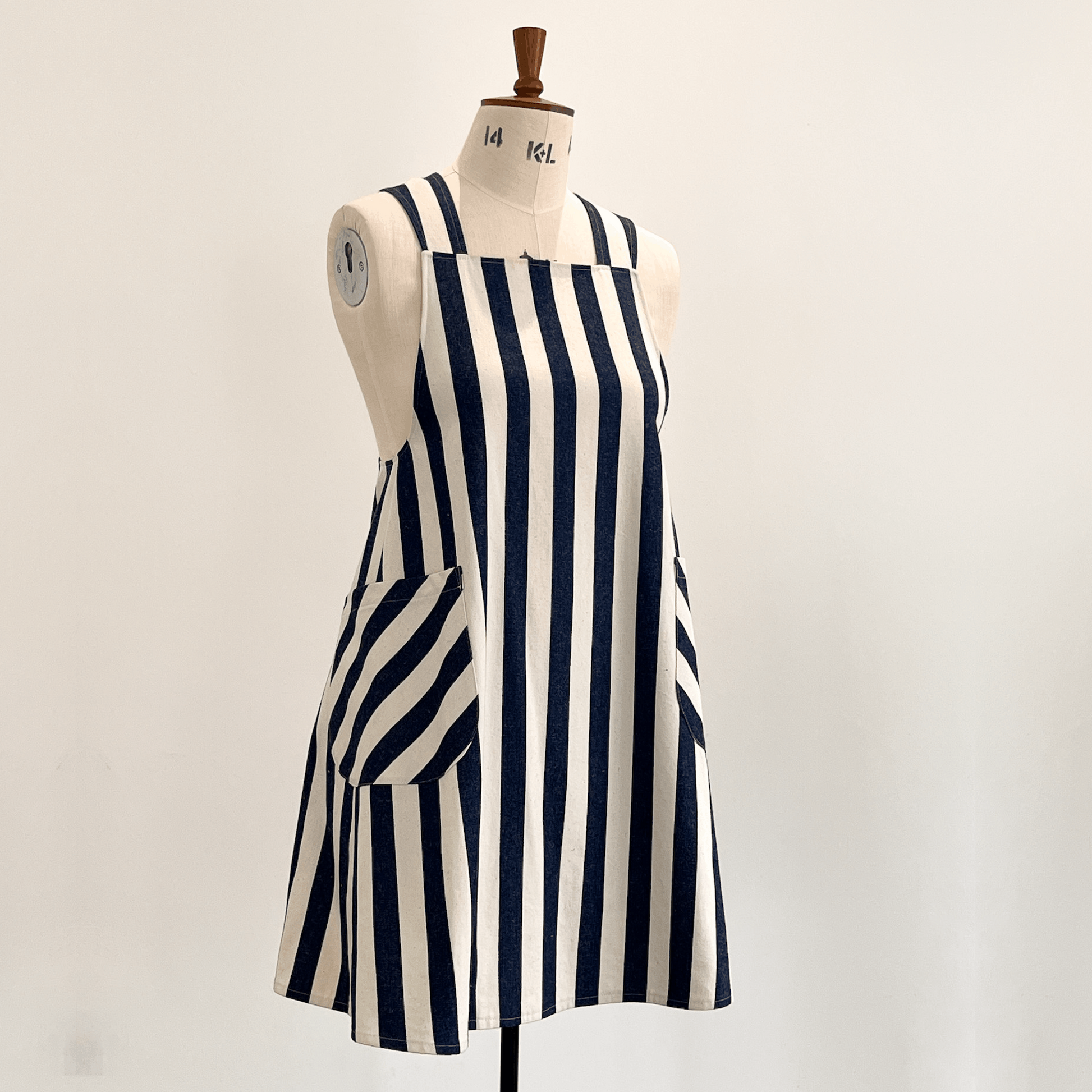 A Japanese style apron with vertical navy blue and off-white stripes, displayed on a cream-coloured dress form mannequin against a plain light background.