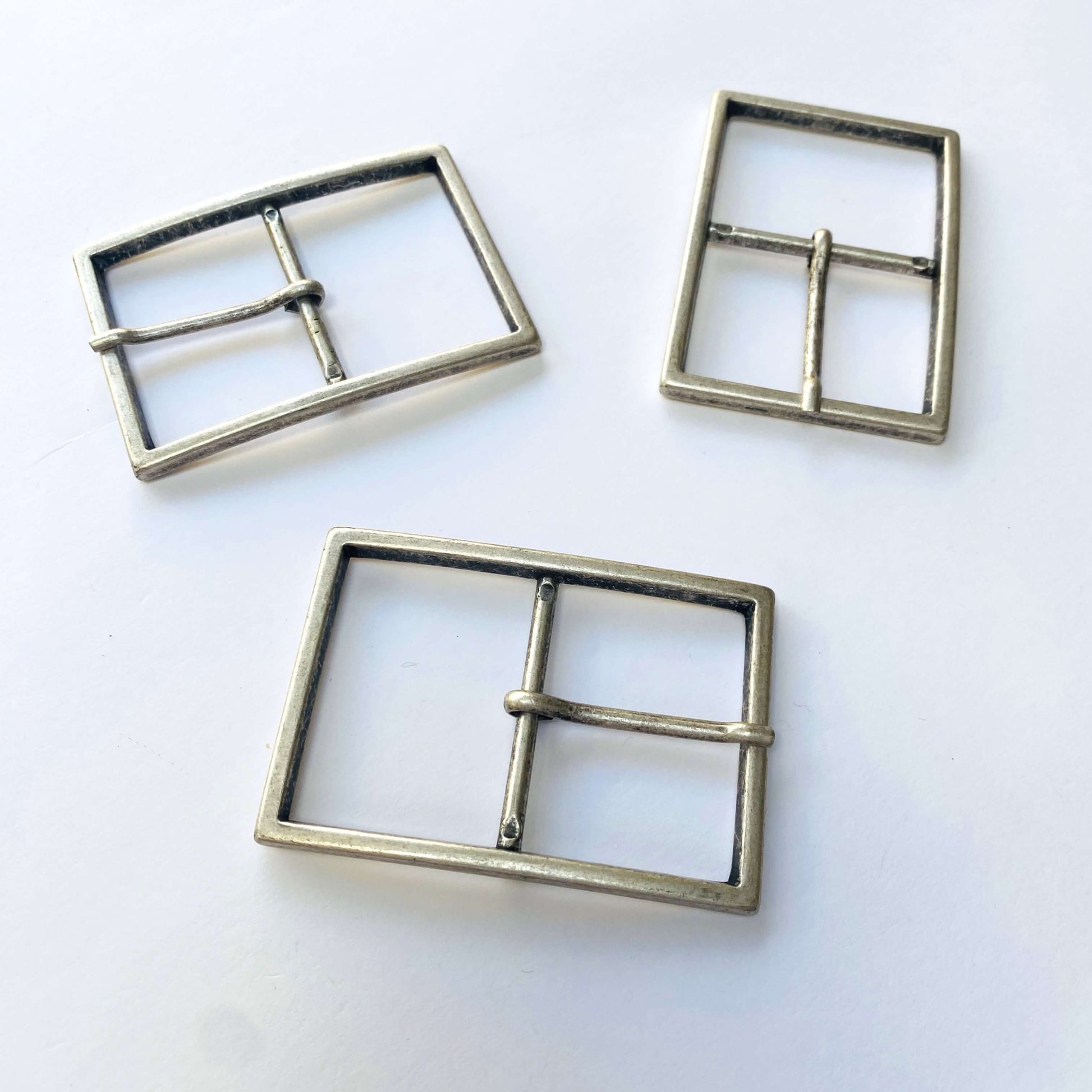Three large antique silver metal belt buckles with prongs on a white background