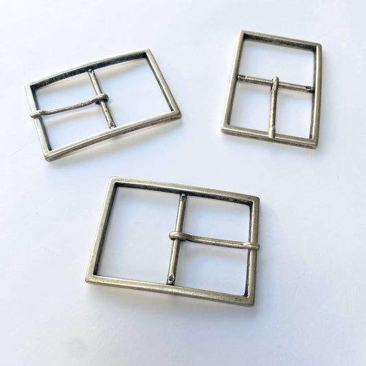 Three large antique silver metal belt buckles with prongs on a white background