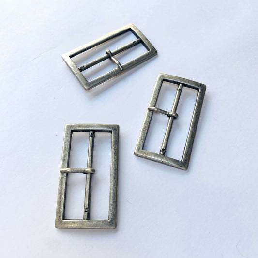 Three metal antique silver belt buckles on a white background