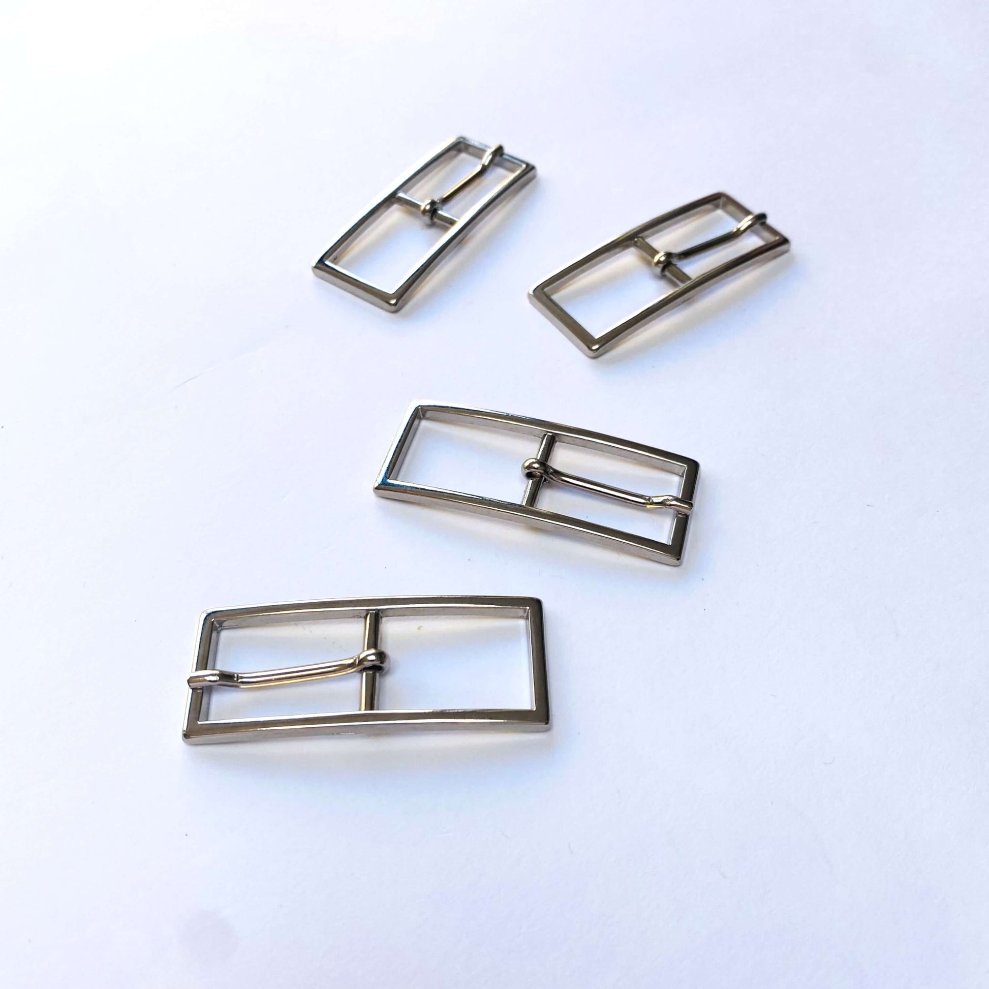 Four silver rectangular buckles with central prong on a white background