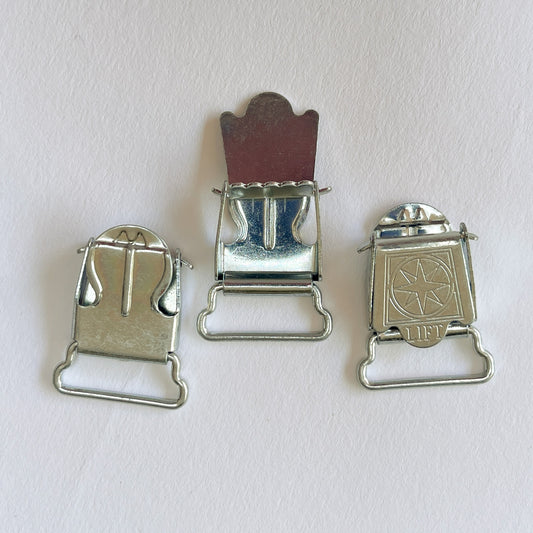 Small silver metal suspender clips or clasps with a star-and-circle emblem on the front, photographed on a plain light background. Can also be used for Braces.