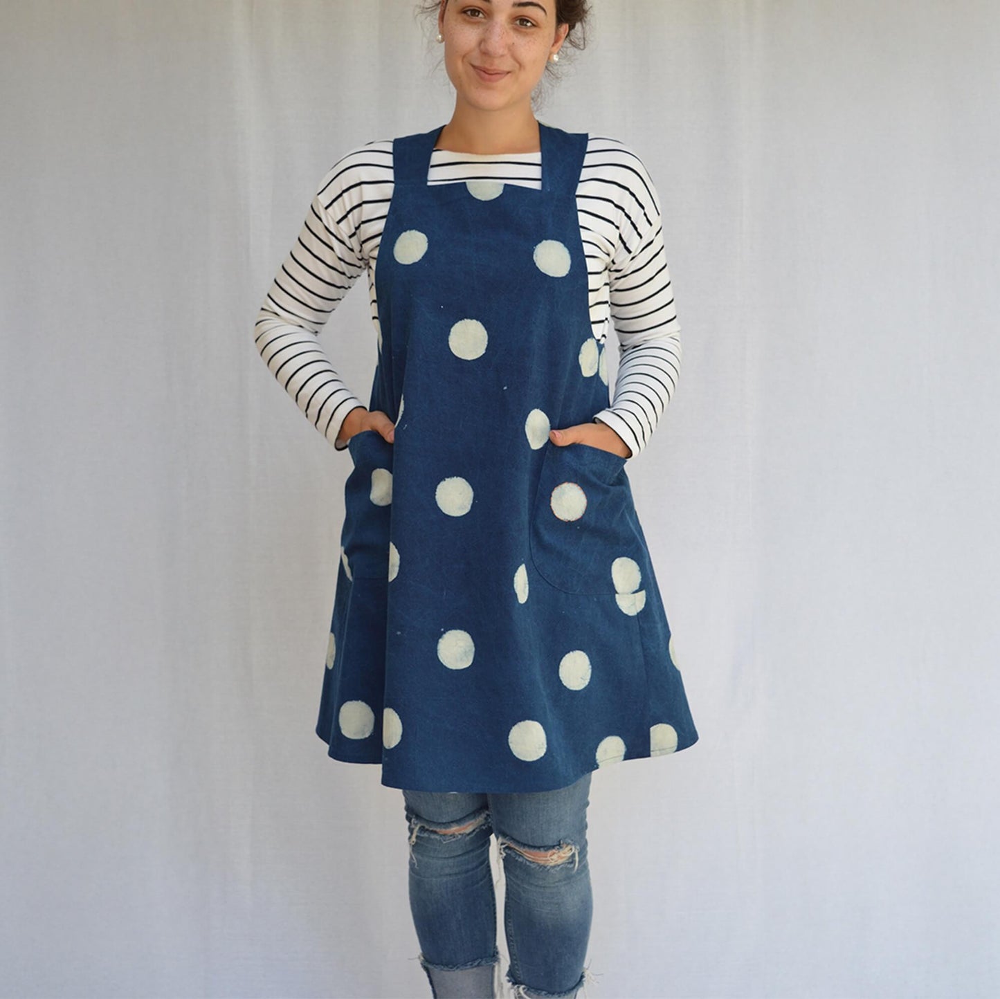 A woman modelling a navy blue linen apron with large white polka dots over a navy and white striped long-sleeve shirt.
