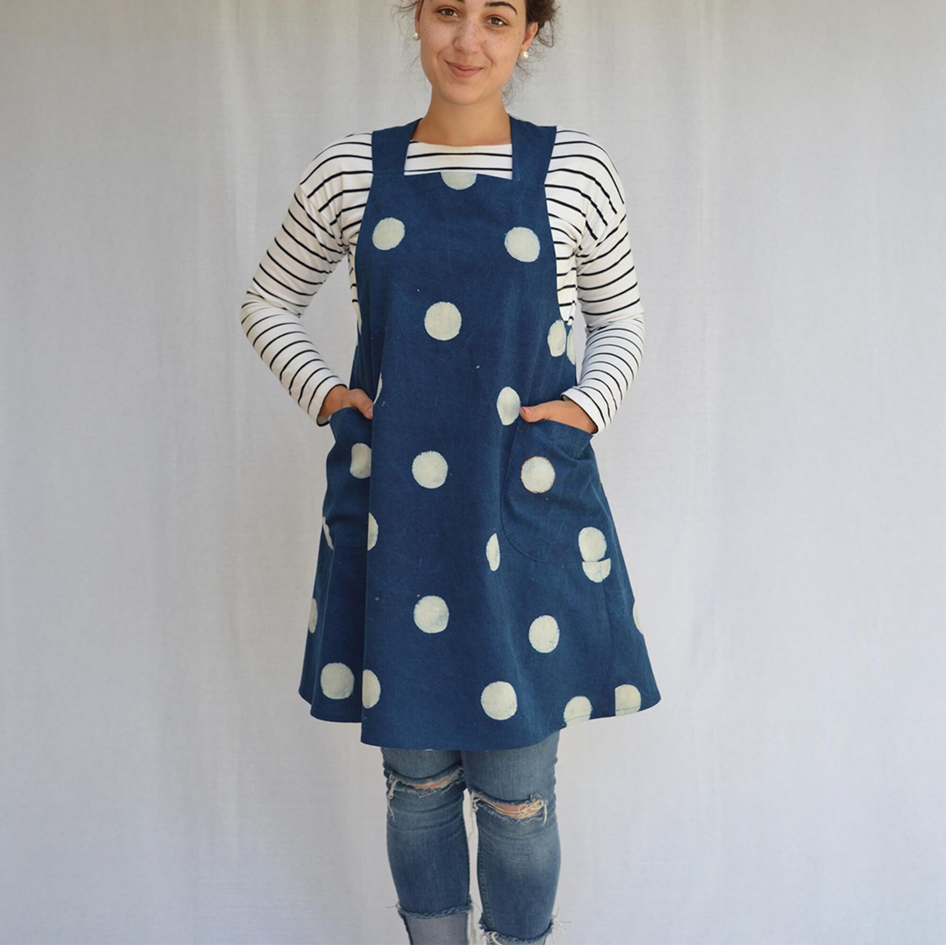 A woman modelling a navy blue linen apron with large white polka dots over a navy and white striped long-sleeve shirt.