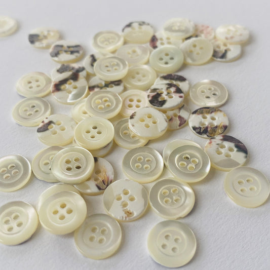 A pile of small round Trocas shell 4-hole ring edge shirt buttons scattered on a plain white surface.