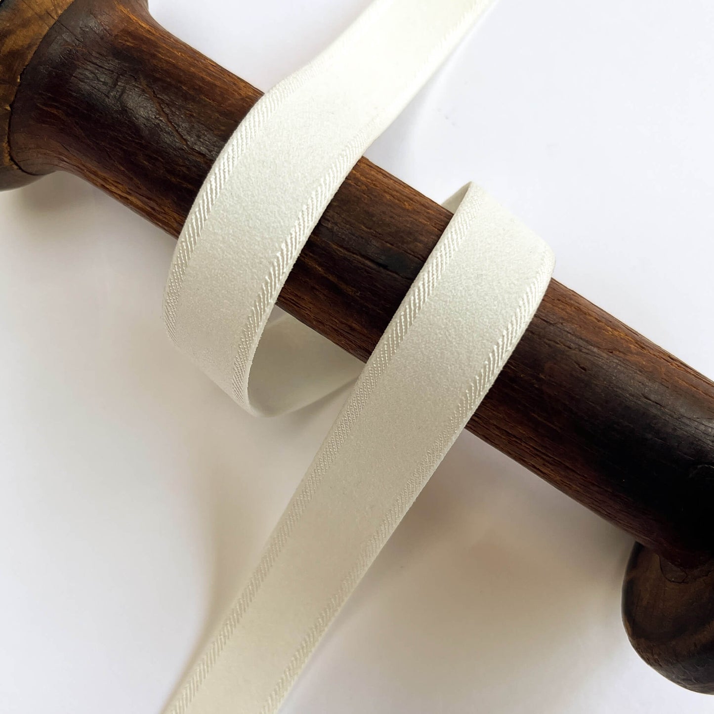 ivory Twill Edge Lingerie Elastic with a fine diagonal herringbone pattern, wrapped around a dark brown wooden dowel on a plain white background.