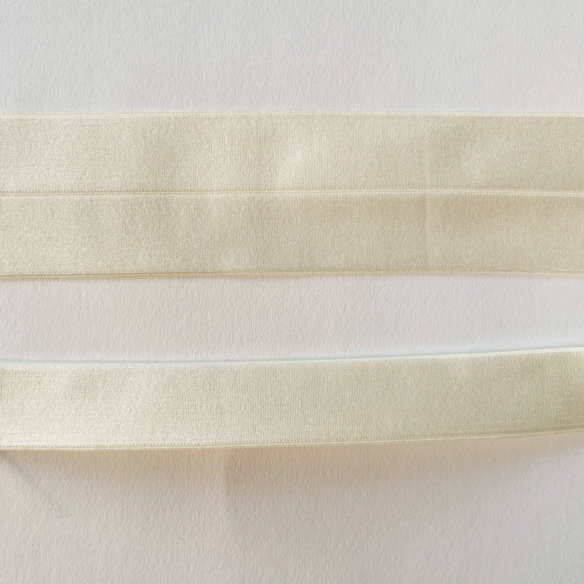 close up of Wide Soft Stretch Satin Fold Over Elastic (FOE) in Ivory, shown flat and folded in half