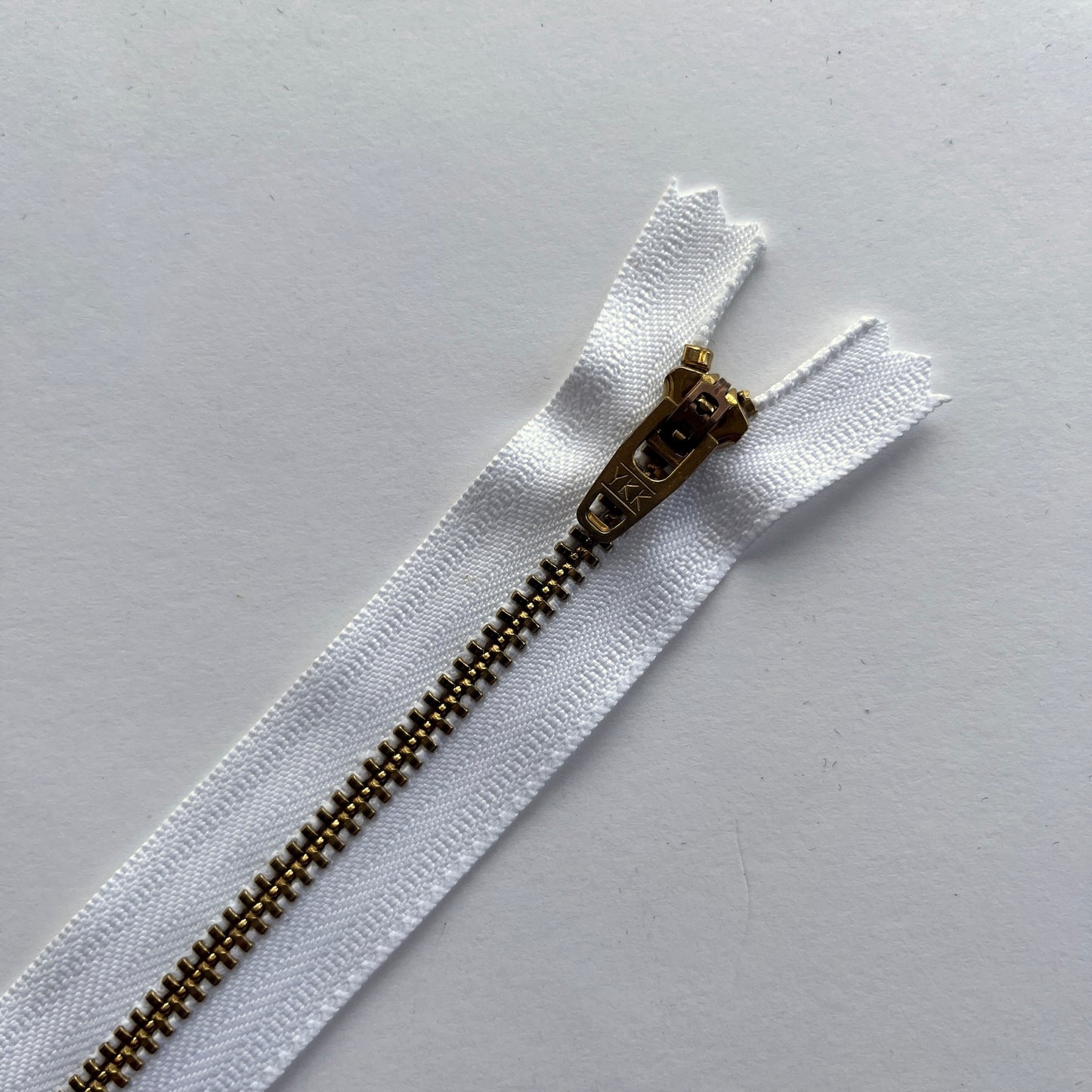close up of YKK white jeans zip with brass metal teeth and auto-lock puller