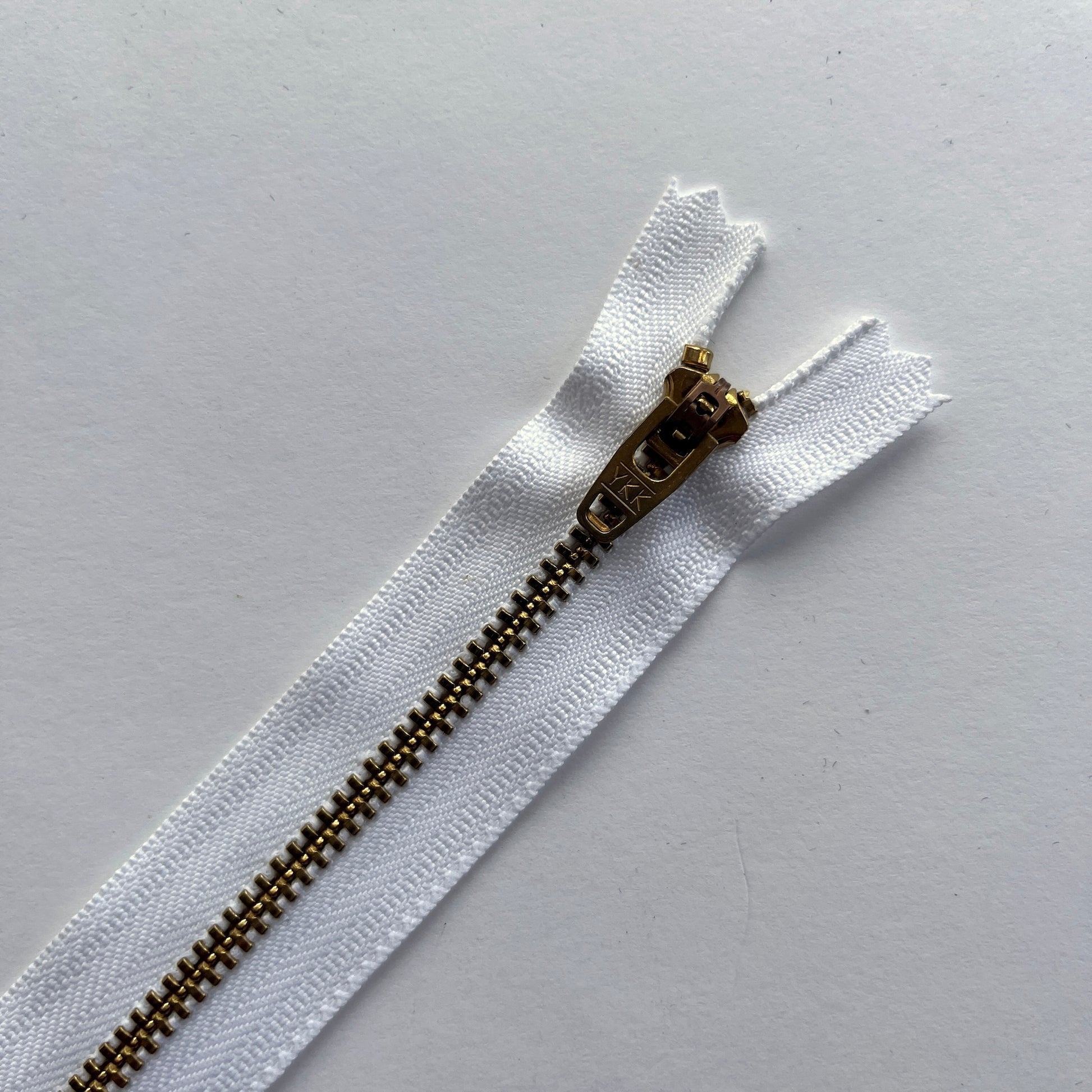 close up of YKK white jeans zip with brass metal teeth and auto-lock puller