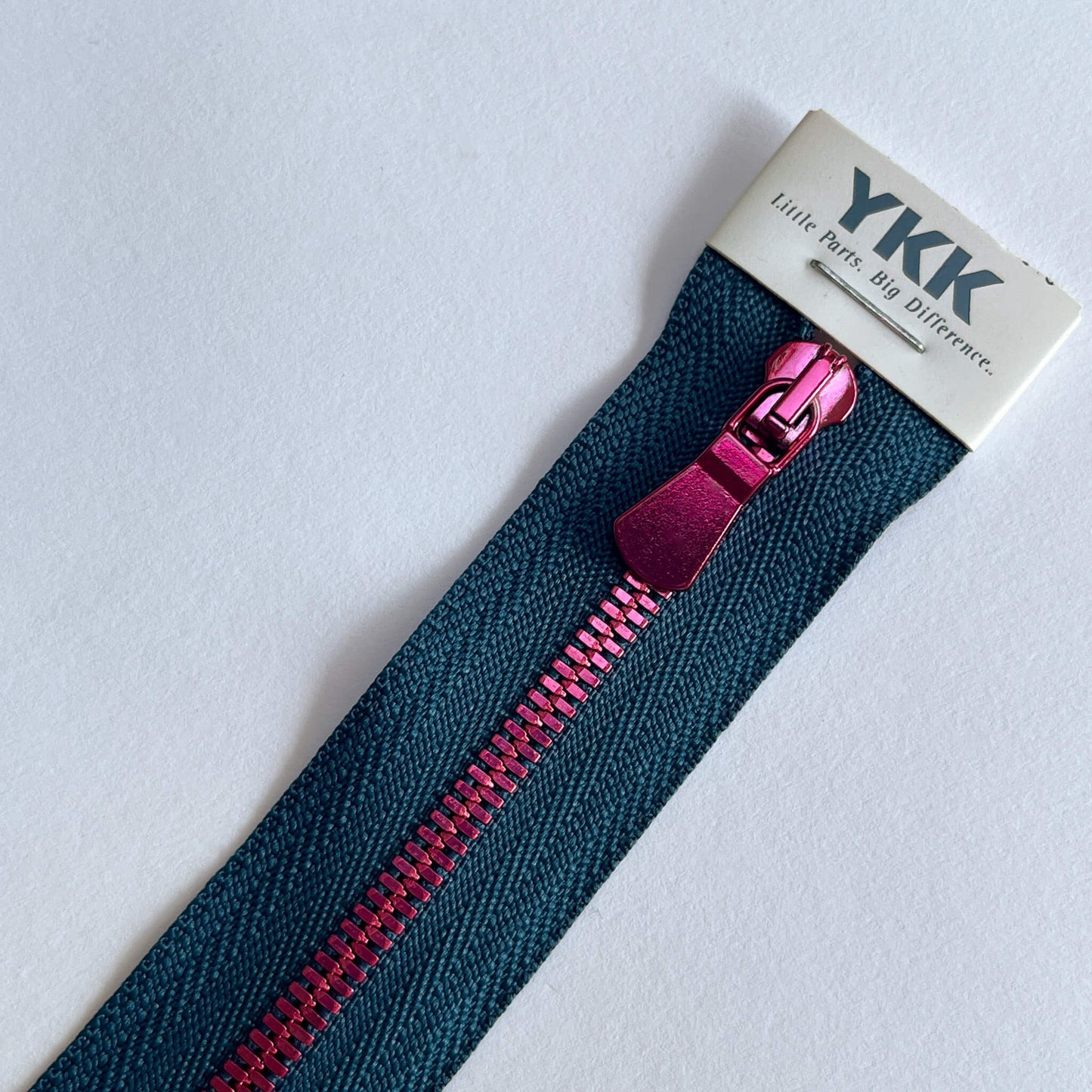 A close-up of a YKK zipper with a dark blue tape and a metallic magenta-pink pull tab