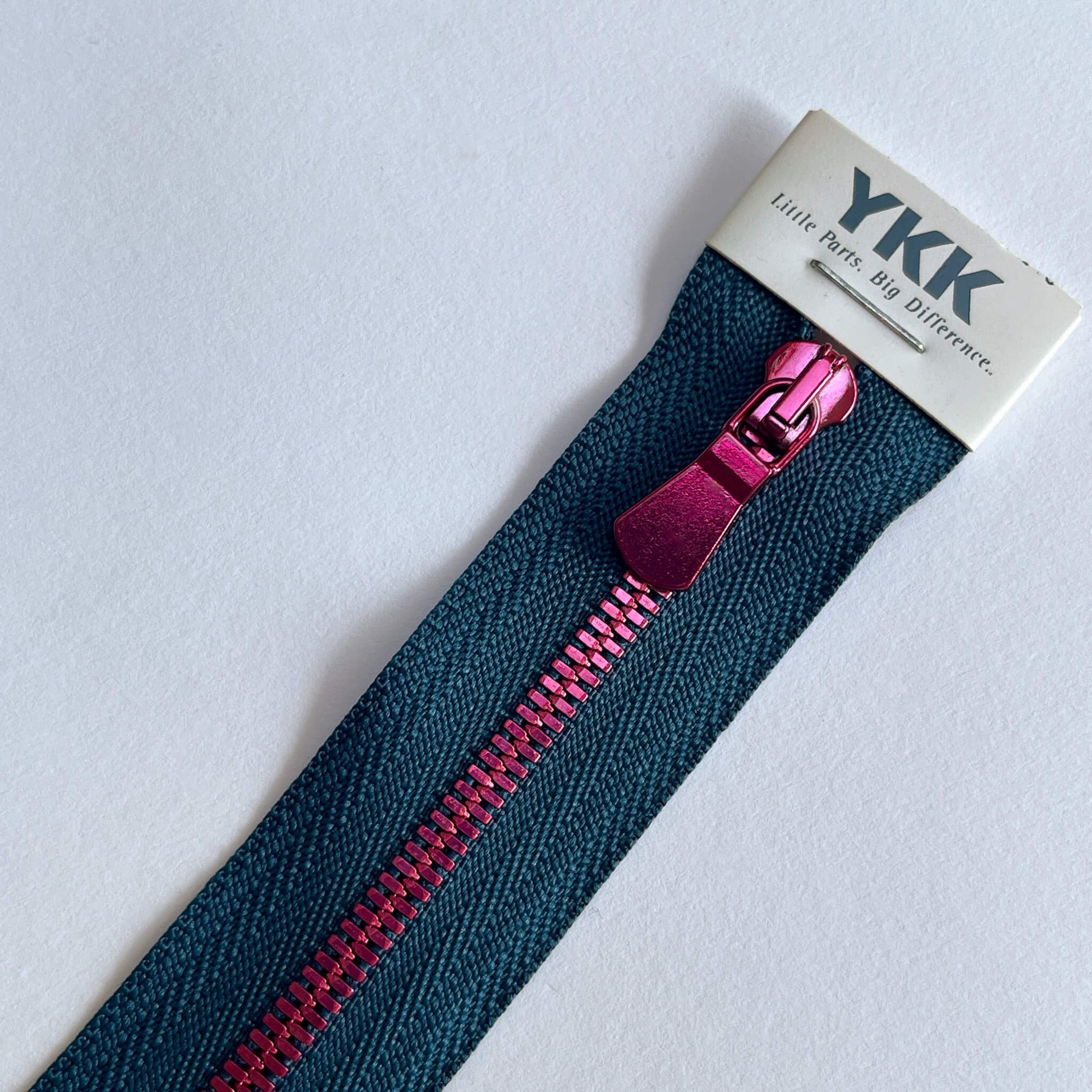 A close-up of a YKK zipper with a dark blue tape and a metallic magenta-pink pull tab