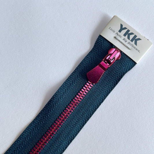 A close-up of a YKK zipper with a dark blue tape and a metallic magenta-pink pull tab