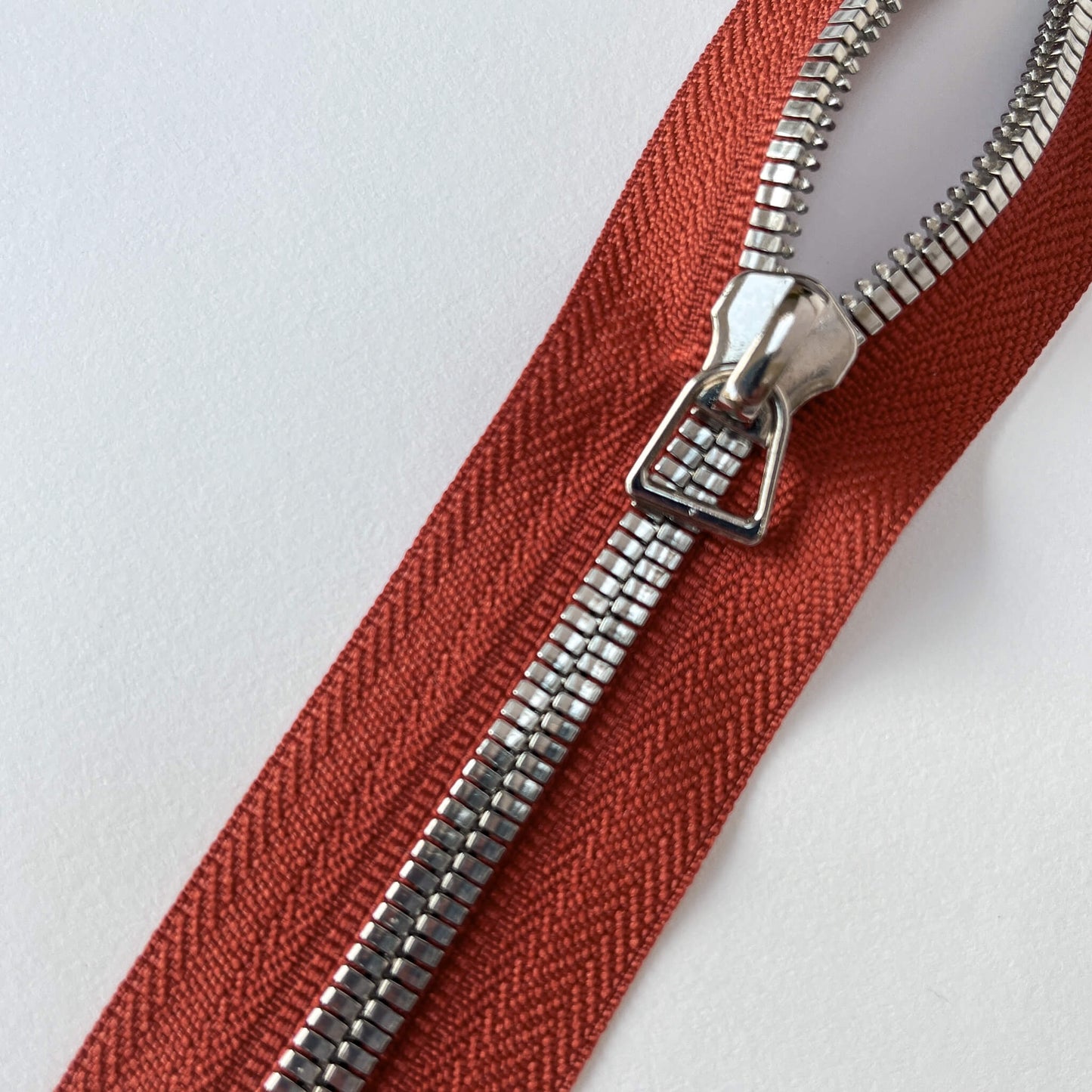 Close up of A YKK EXCELLA® Flat closed end zip with Rusttape, flat, smooth style metal teeth and stirrup puller. 