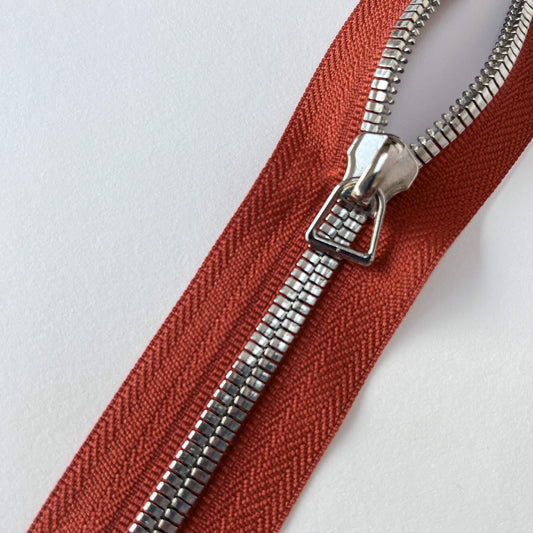 Close up of A YKK EXCELLA® Flat closed end zip with Rusttape, flat, smooth style metal teeth and stirrup puller. 