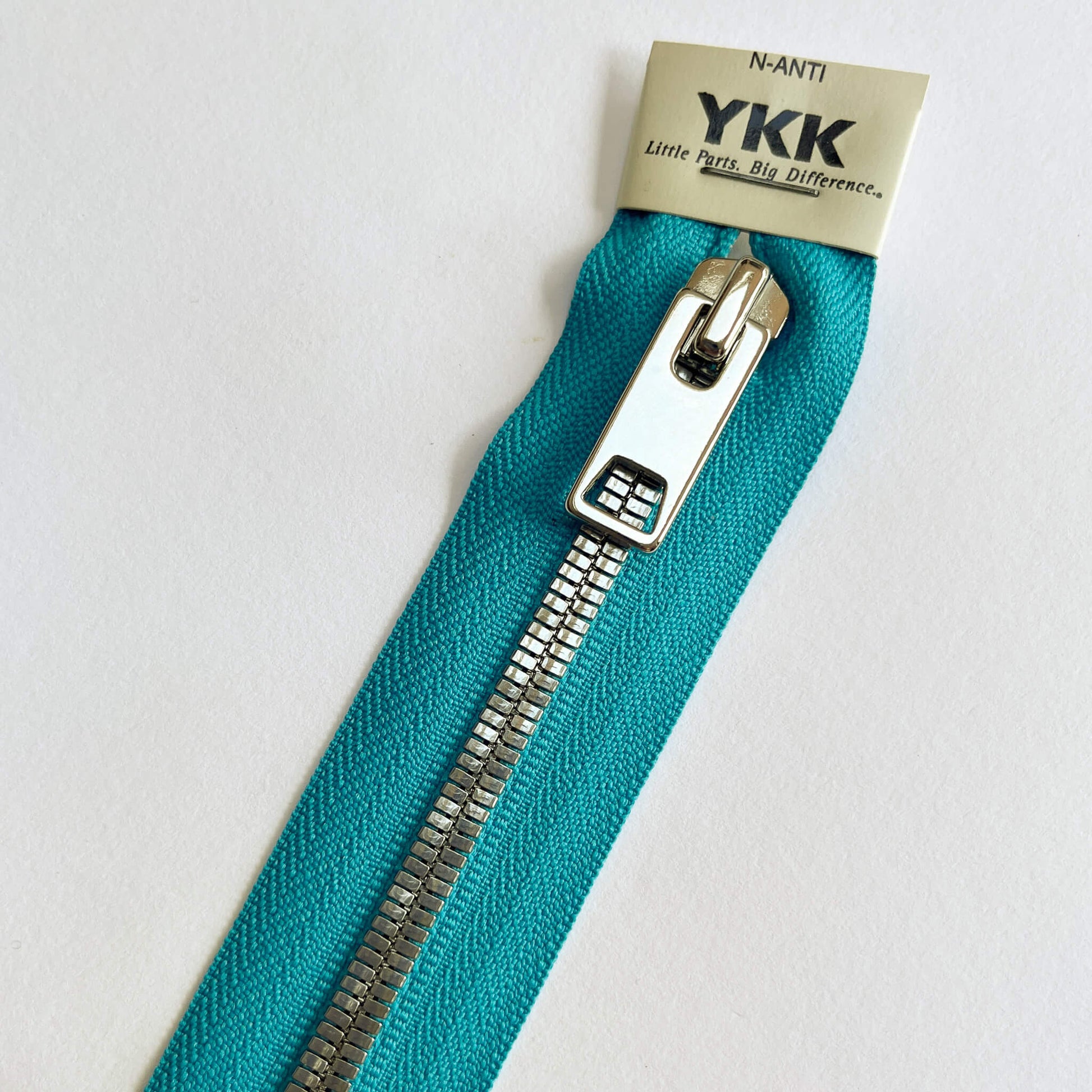close up of Turquoise A YKK EXCELLA® Flat closed end zip with  flat, smooth style silver metal teeth and decorative puller. 