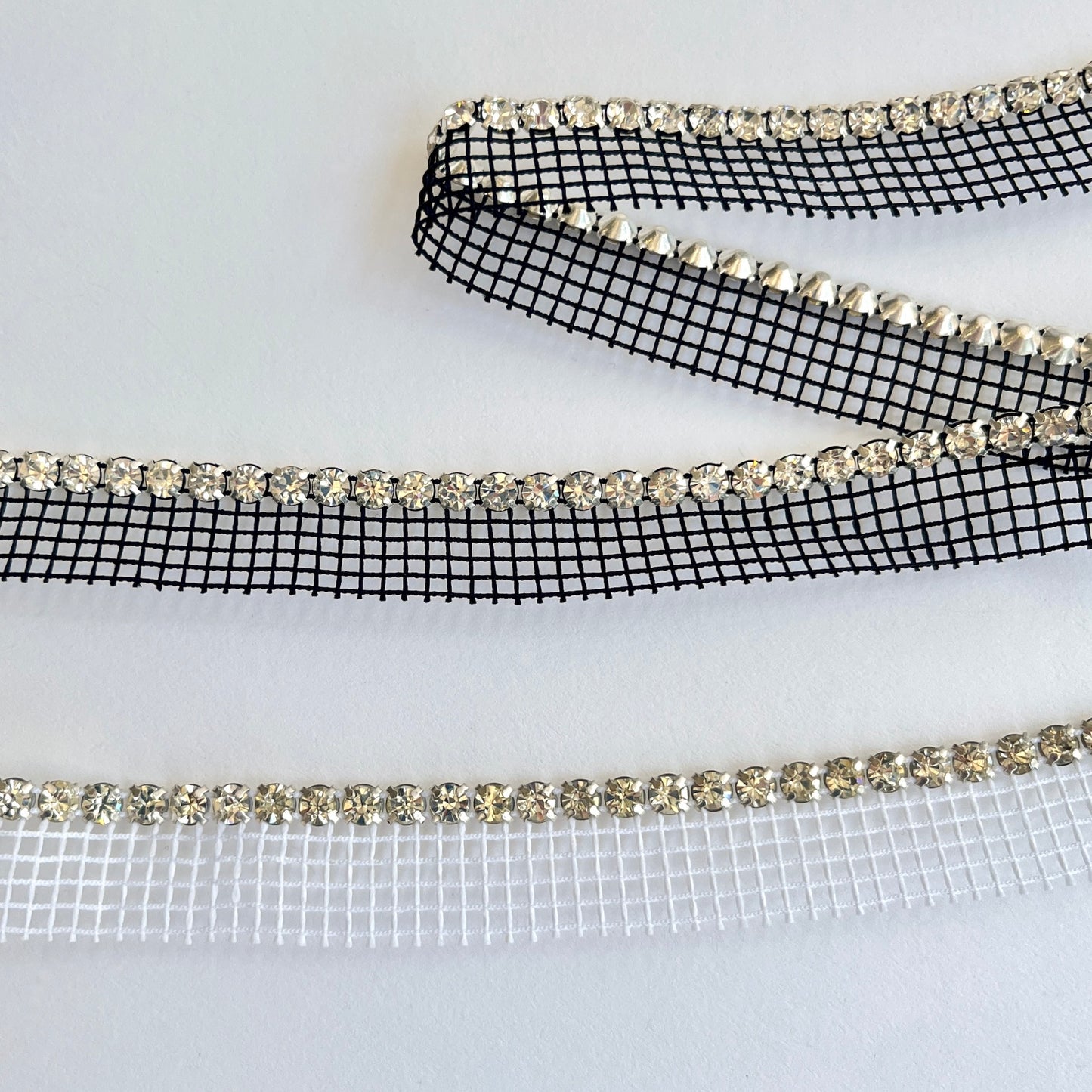 Sparkly rhinestone insertion trim - premium high grade diamanté crystals on a flexible net insertion tape. Please note - we have very limited stock of the white colour way.  Black/clear crystal: Sold by the metre  White/clear crystal: LIMITED STOCK - 80cm length only